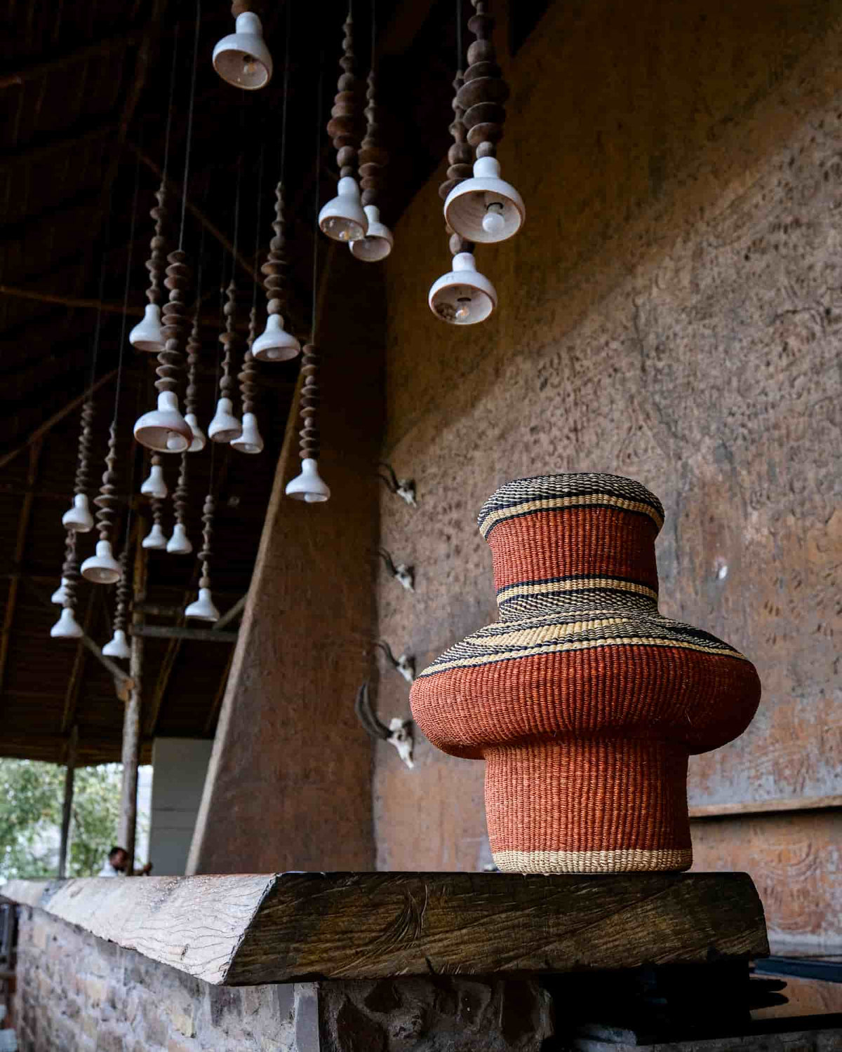 Sculptural terracotta Bolga art basket with black and natural bands displayed on a wooden beam.