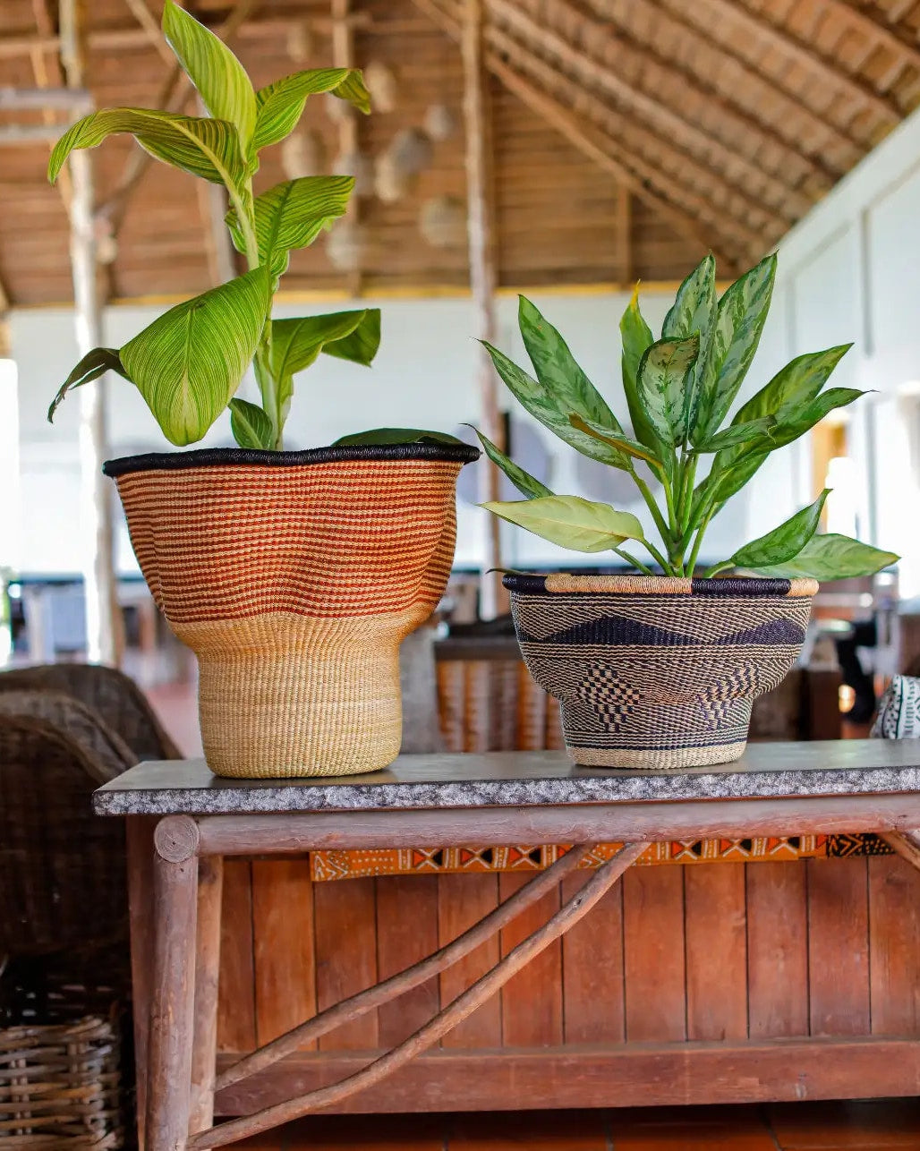 Sculptural basket sitting on a table inside a large room with foliage and wooden roof