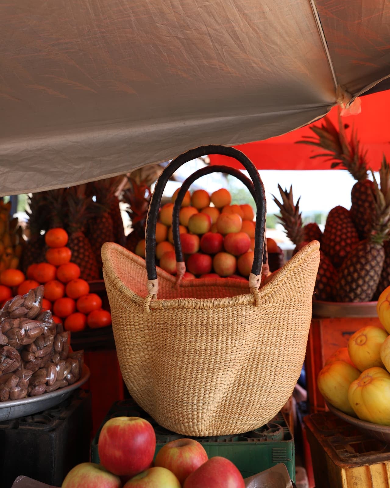 A wavy natural basket filled with and surrounded by tomatoes sitting on black plastic