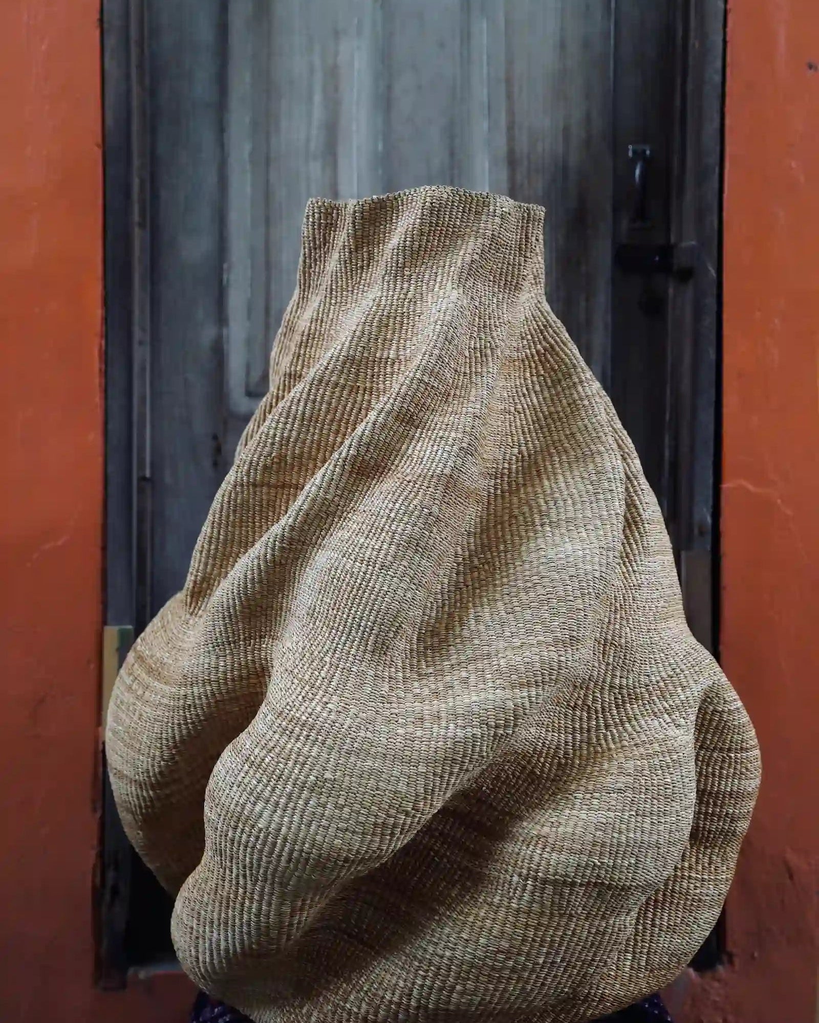 Large, sculptural wavy basket sitting on a black and white cloth in front of a wooden door
