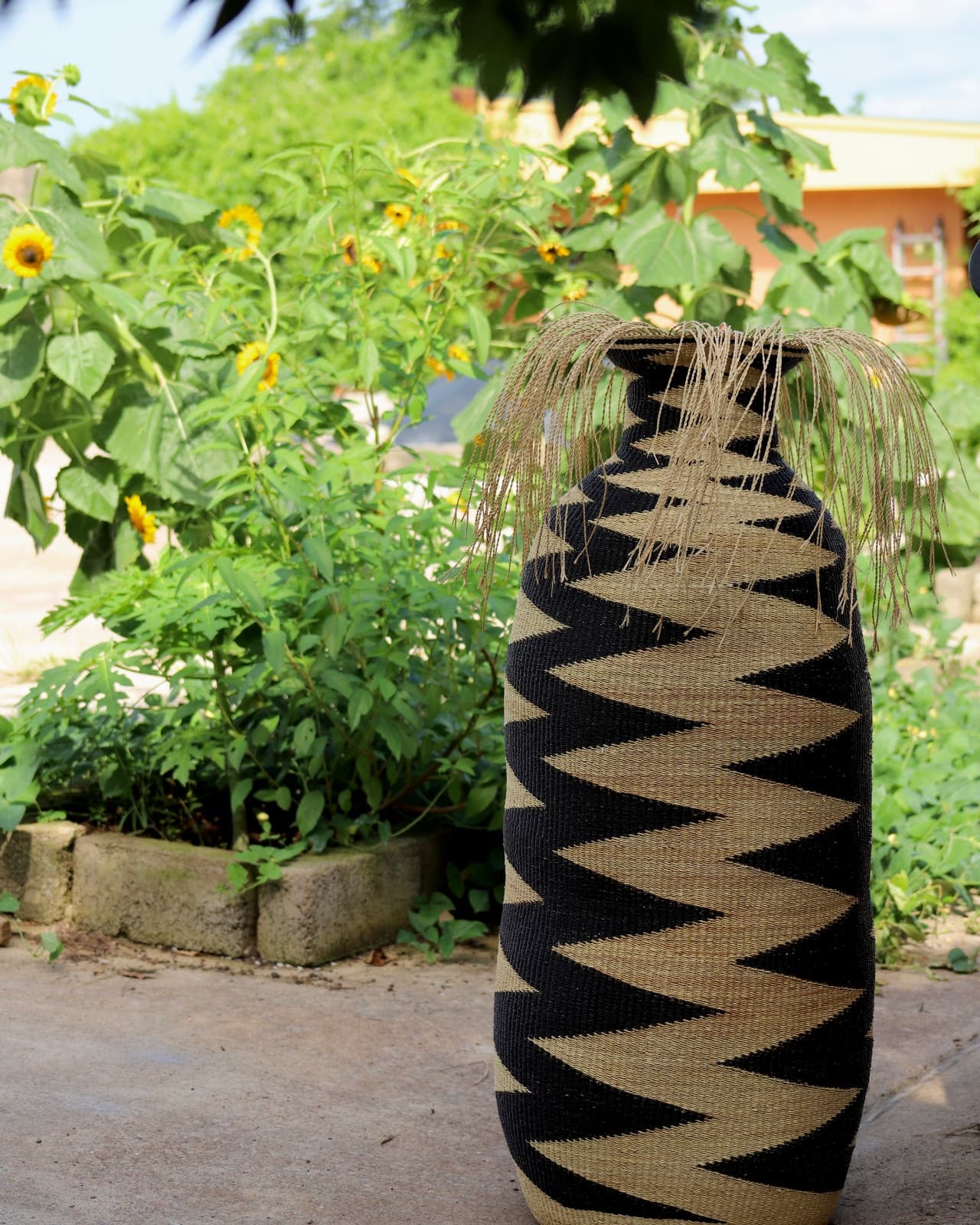 Large patterned basket sitting on concrete with green foliage in the background