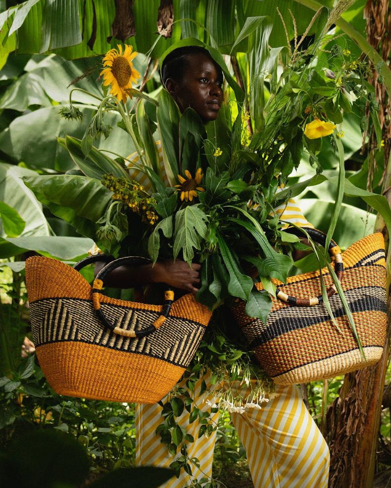 Woman holding two colourful baskets filled with plants with green foliage in the background