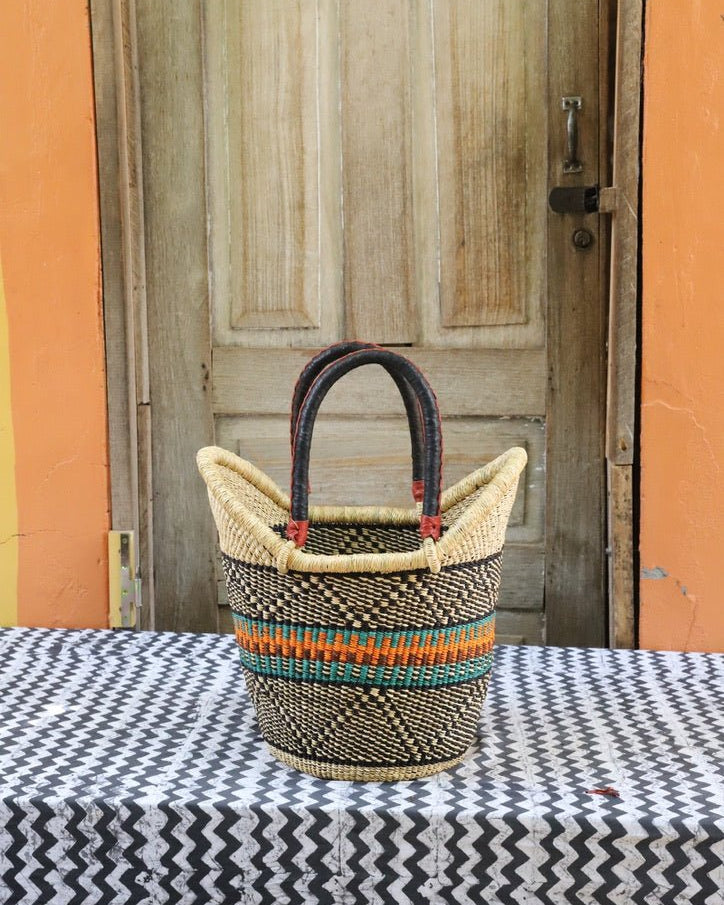 Woven basket with colorful handles on a tablecloth in front of a wooden door.