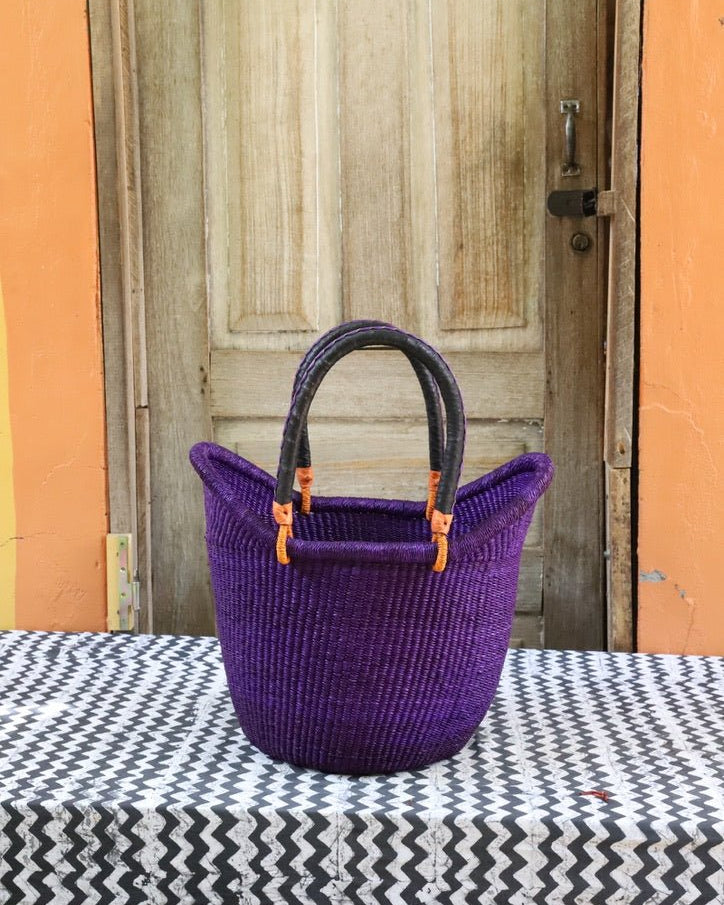 Purple woven basket with black handle on a table in front of a wooden door.