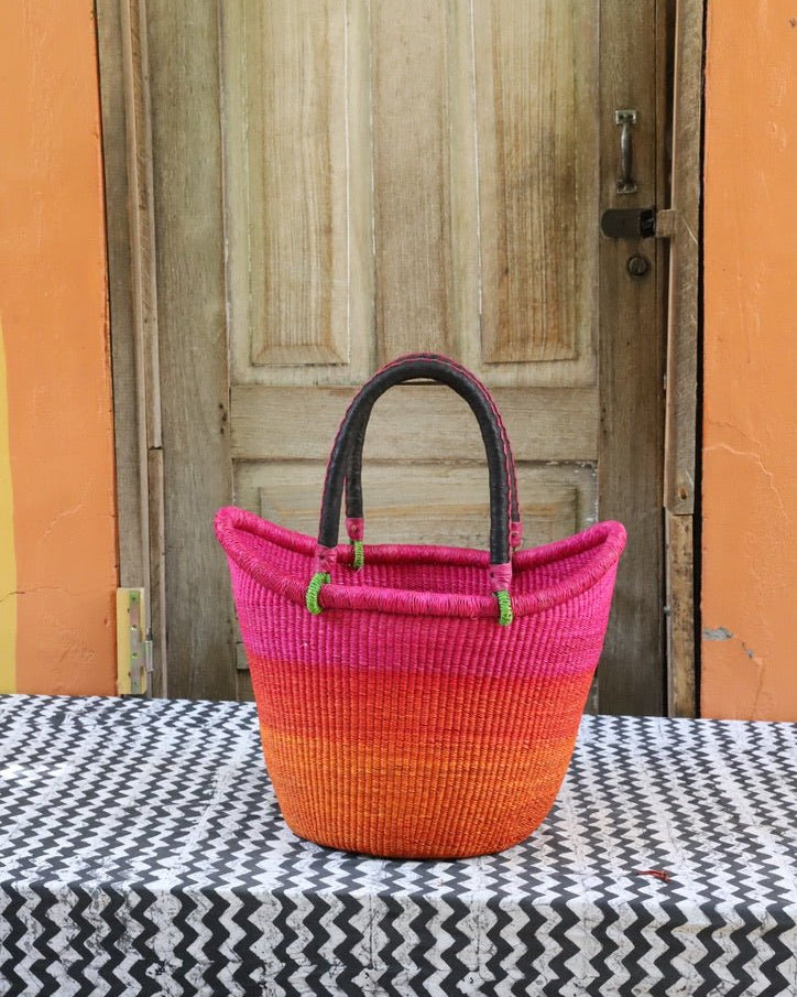 Woven basket with pink and orange gradient on a black and white patterned tablecloth, wooden door in the background.