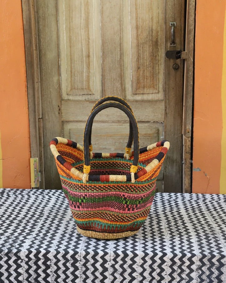 Woven carry on basket with premium leather on a black and white cloth against a wooden door