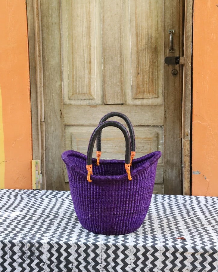 Purple woven basket with black handles on a table in front of a wooden door.