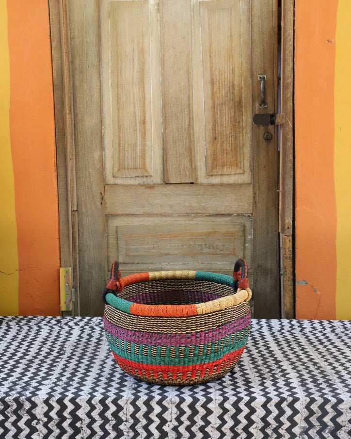 A colorful handwoven storage basket sitting on a black and white cloth against a wooden door