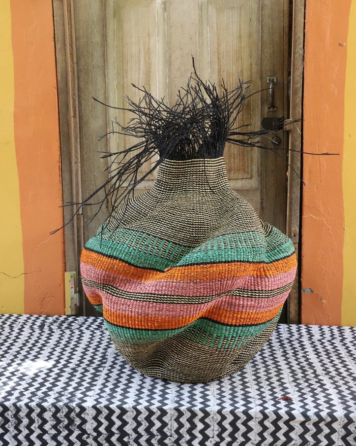 Multicolored woven vase on a table with a wooden door and colorful wall in the background