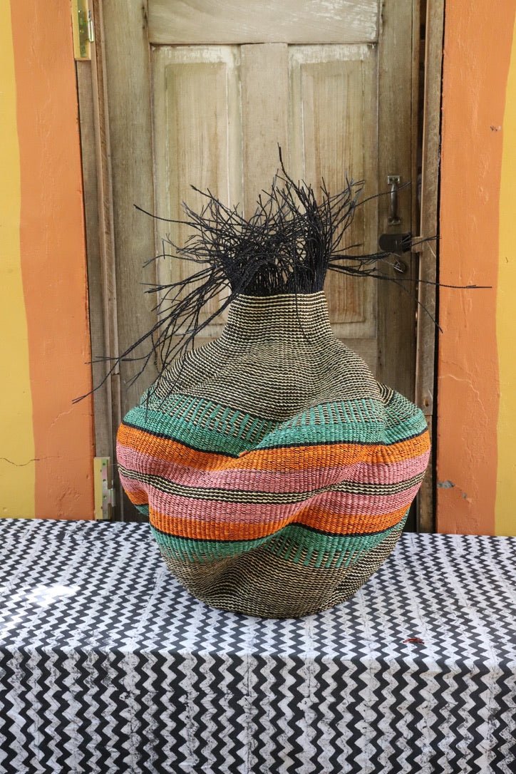 A colorful, handwoven piece sitting on a black and white cloth with decorative straw branching out.