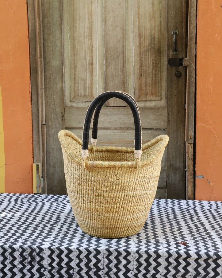 Woven basket with black handles on a tablecloth in front of a wooden door.
