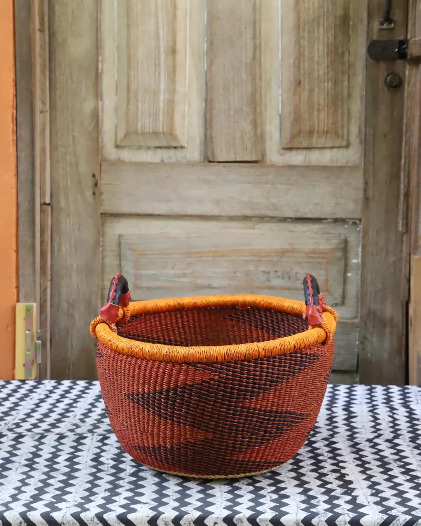 A colorful handwoven storage basket sitting on a black and white cloth against a wooden door