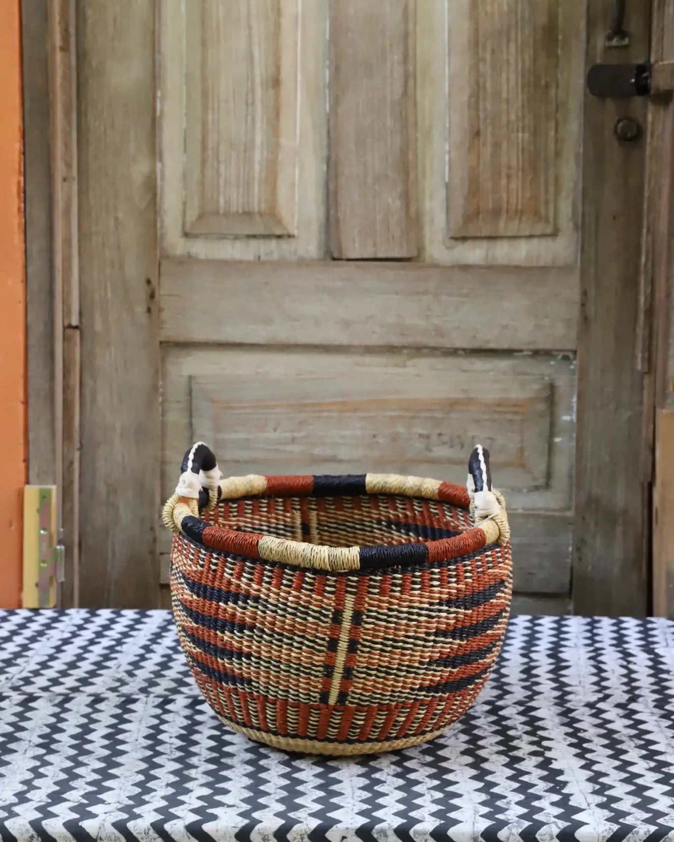 A handwoven storage basket sitting on a black and white cloth against a wooden door