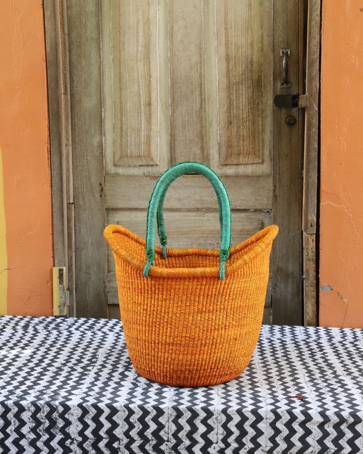 Orange woven basket with green handles on a tablecloth in front of a wooden door.