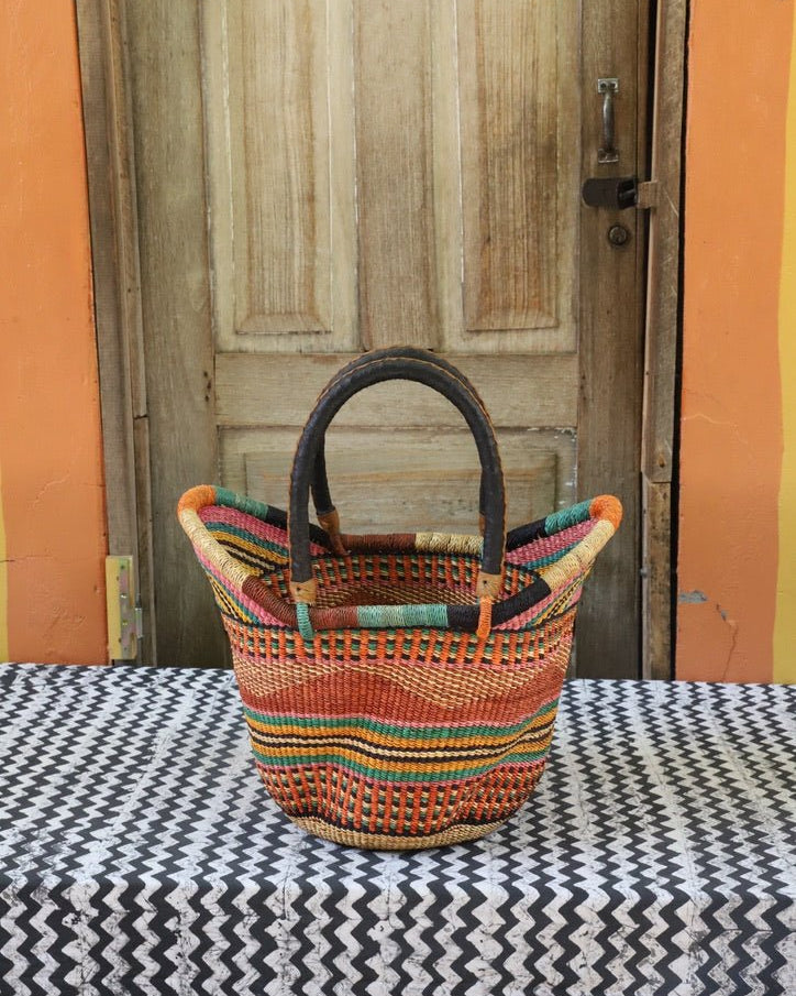 Woven carry on basket with premium leather on a black and white cloth against a wooden door