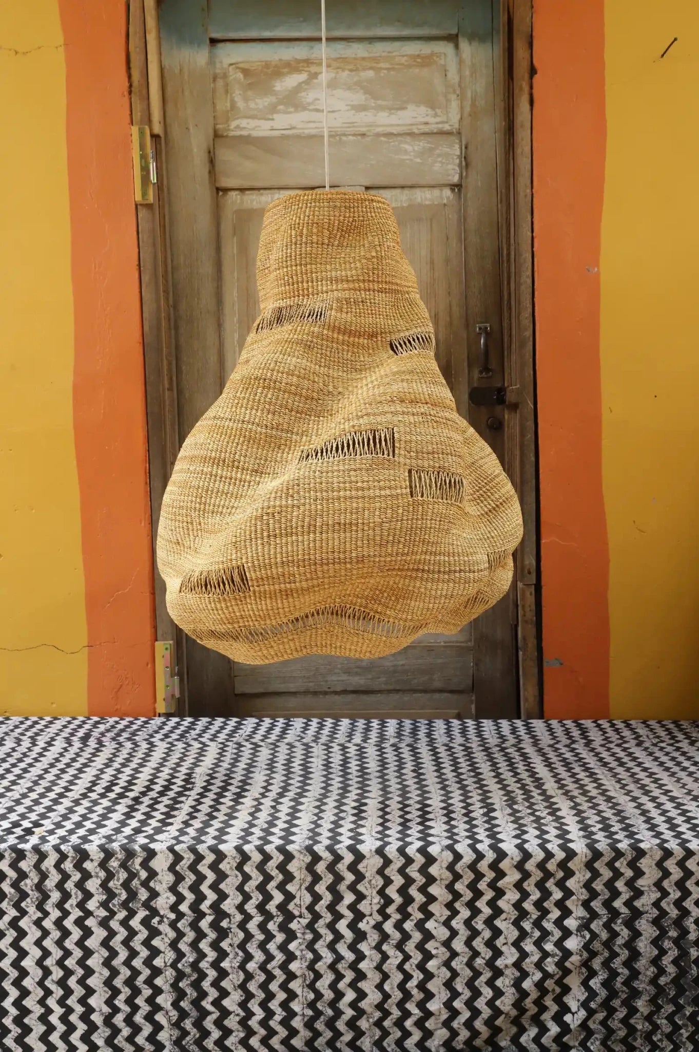 Woven basket hanging above a table with a patterned tablecloth against a yellow wall.