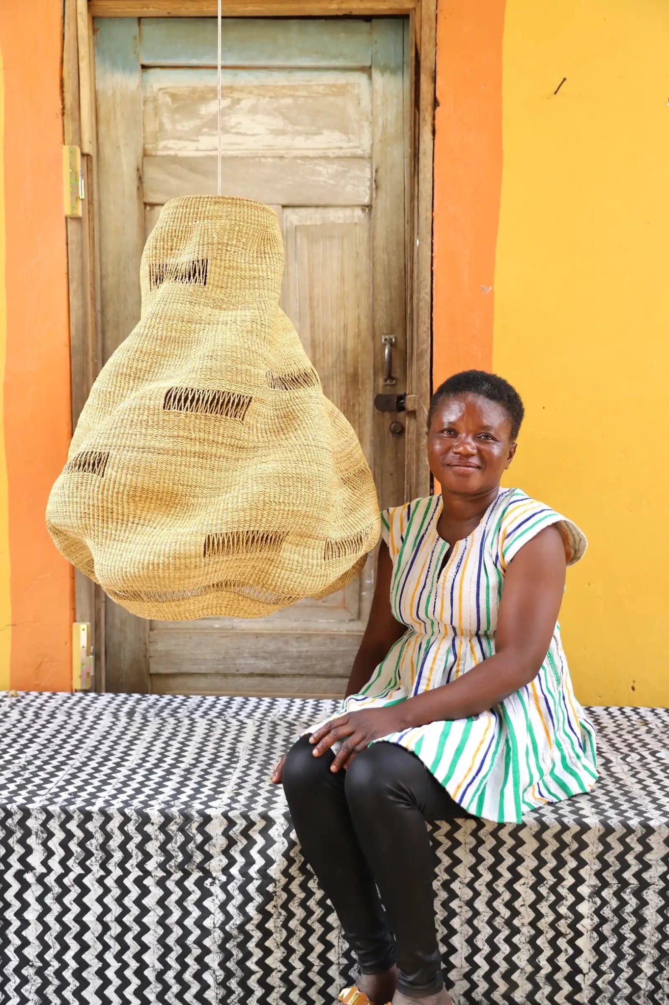 Woman sitting on a bench with a woven basket in front of a colorful wall.
