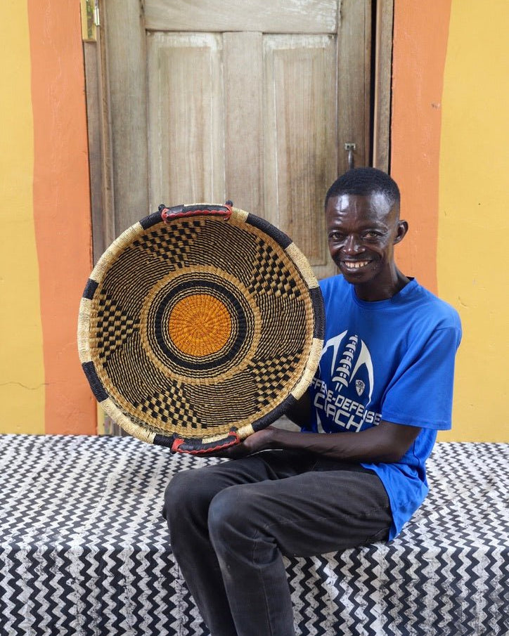 Man holding a woven basket in front of a wooden door with a yellow wall.