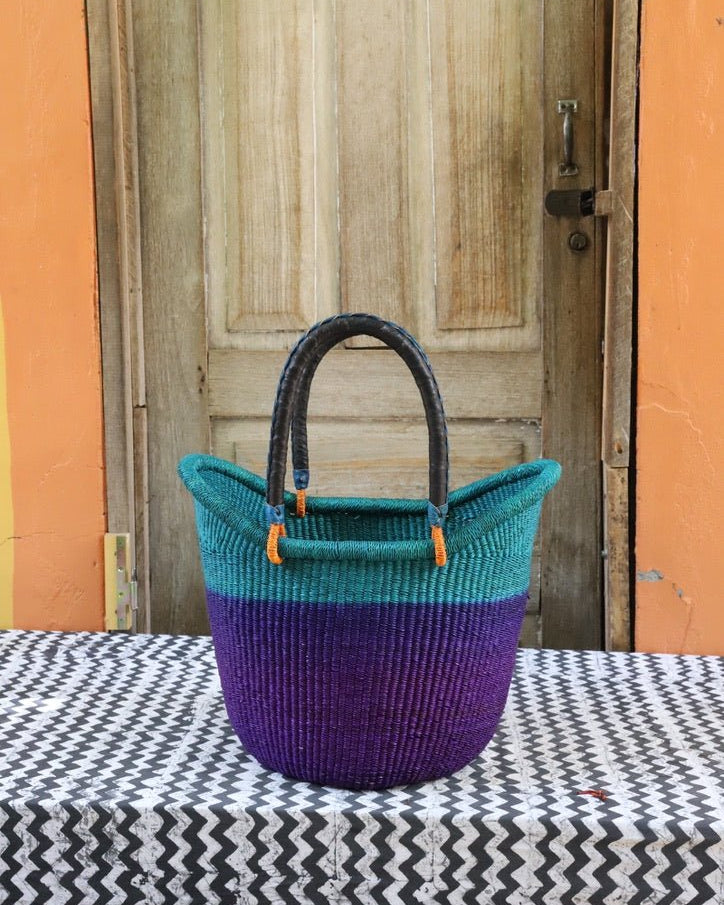 Woven handbag with teal top and purple bottom on a table with a wooden door in the background.