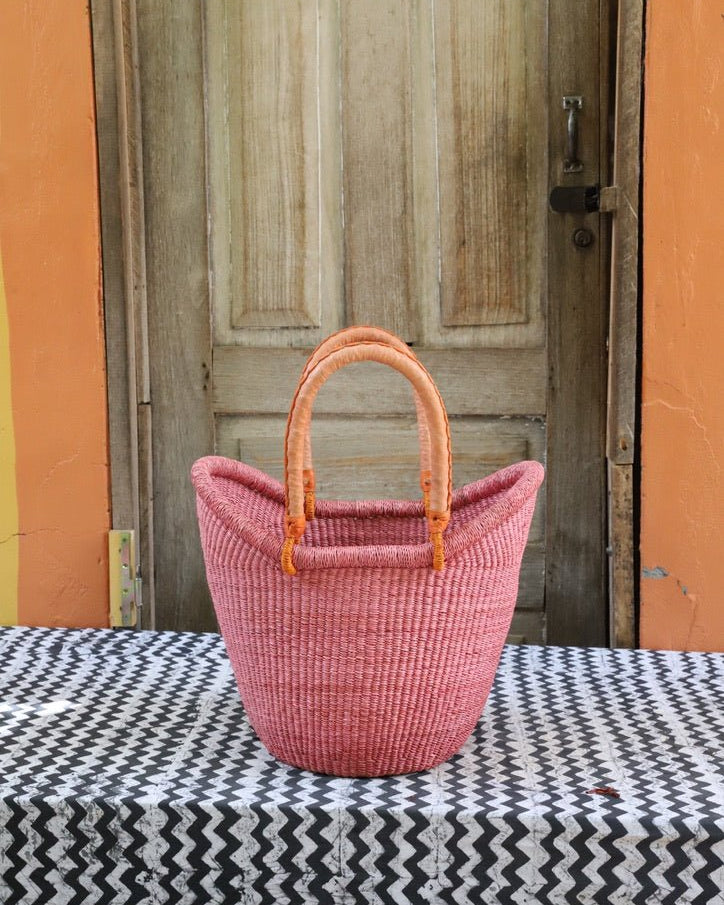 Pink woven basket with wooden handles on a black and white patterned tablecloth in front of a wooden door.