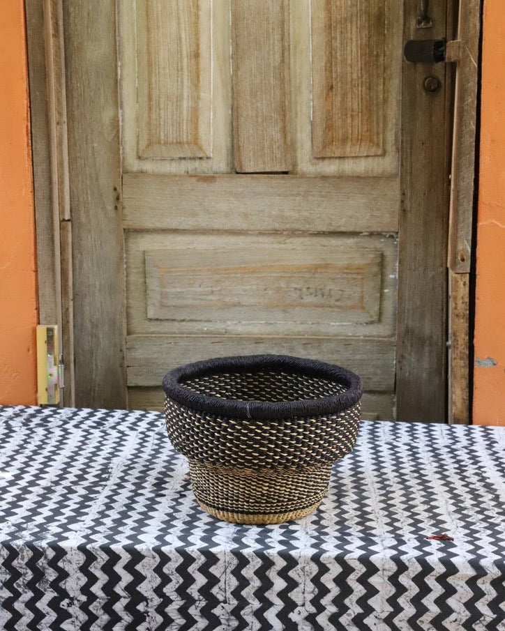 Woven storage basket with a beautiful pattern on a black and white cloth against a wooden door.