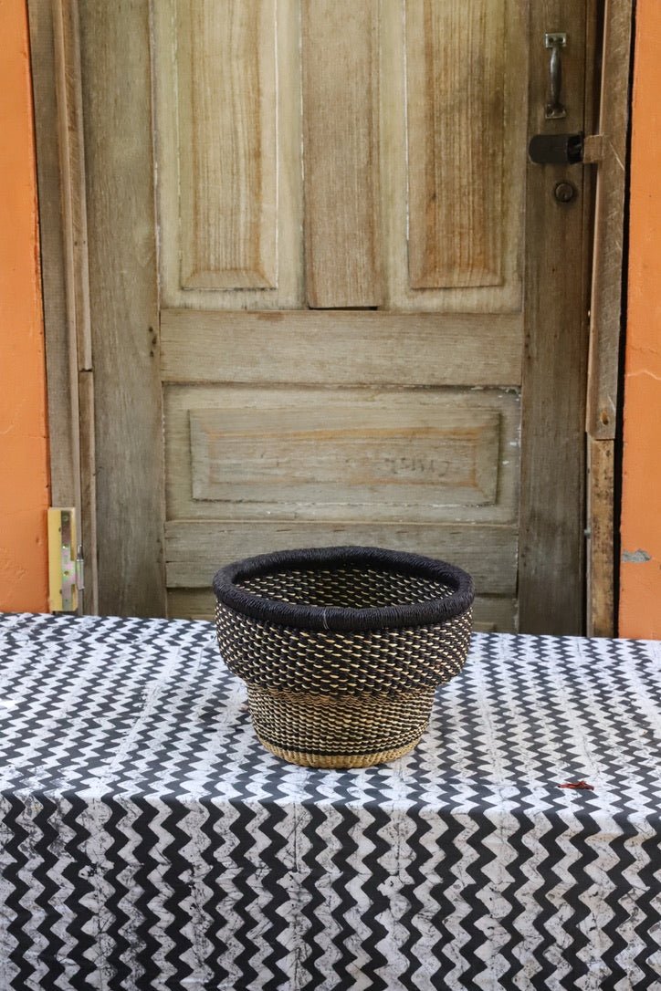 Woven basket on a table with a patterned tablecloth in front of a wooden door.