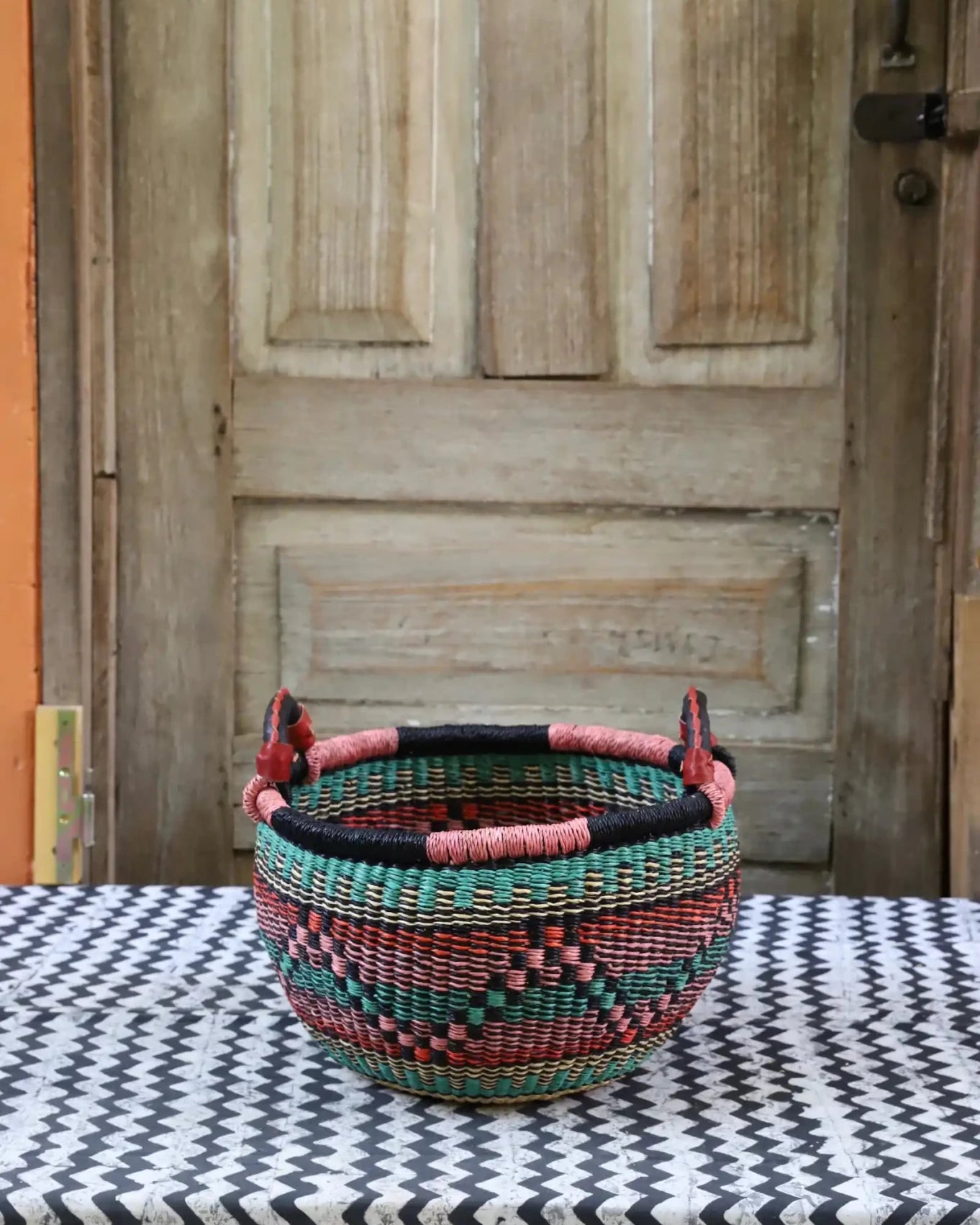 A colorful handwoven storage basket sitting on a black and white cloth against a wooden door