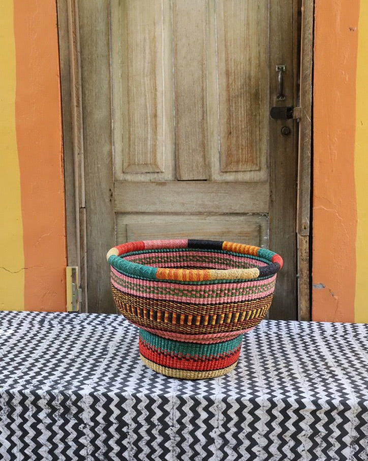 Colorful woven basket on a black and white patterned tablecloth with a wooden door in the background.