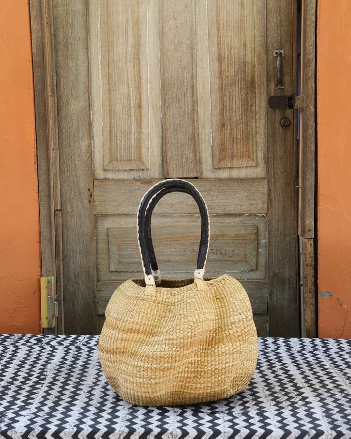 Woven carry on basket with premium leather on a black and white cloth against a wooden door
