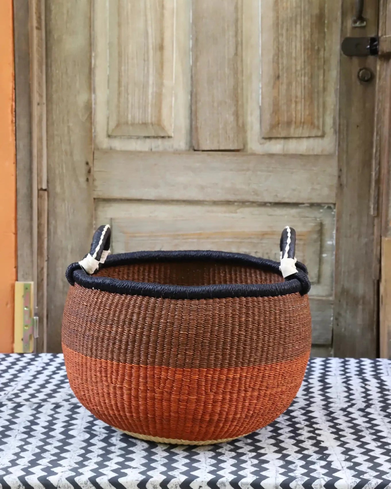 A colorful handwoven storage basket sitting on a black and white cloth against a wooden door