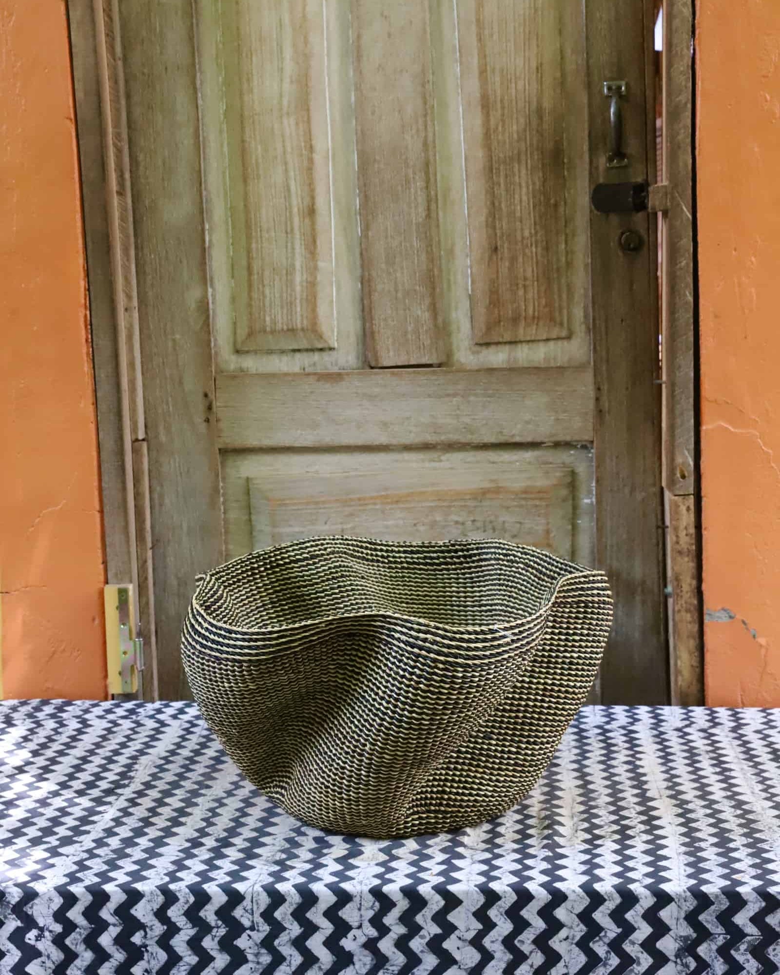Decorative woven basket on a black and white cloth against a wooden door.