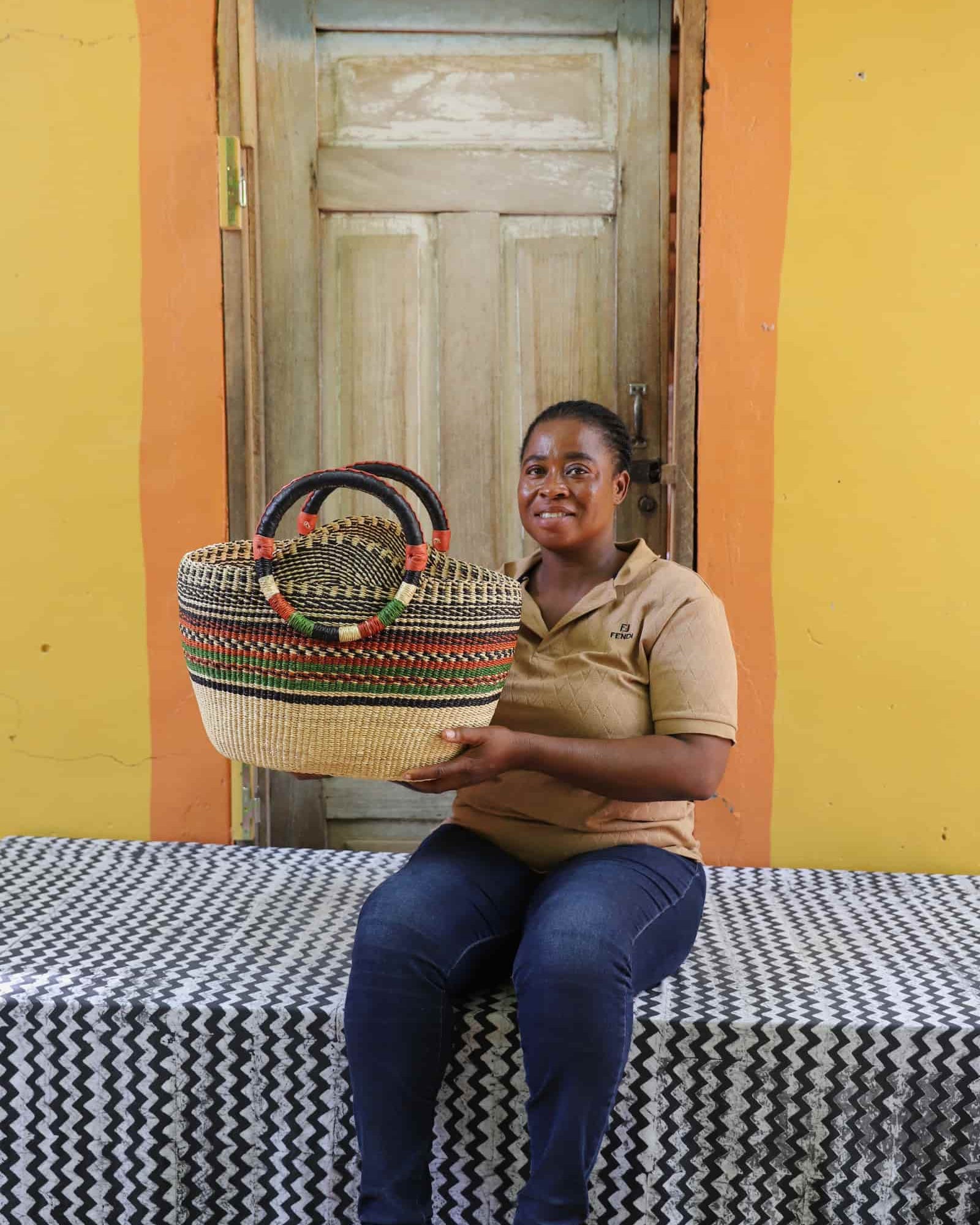 Woman holding a colorful woven carry on bag on a black and white cloth against a wooden door.