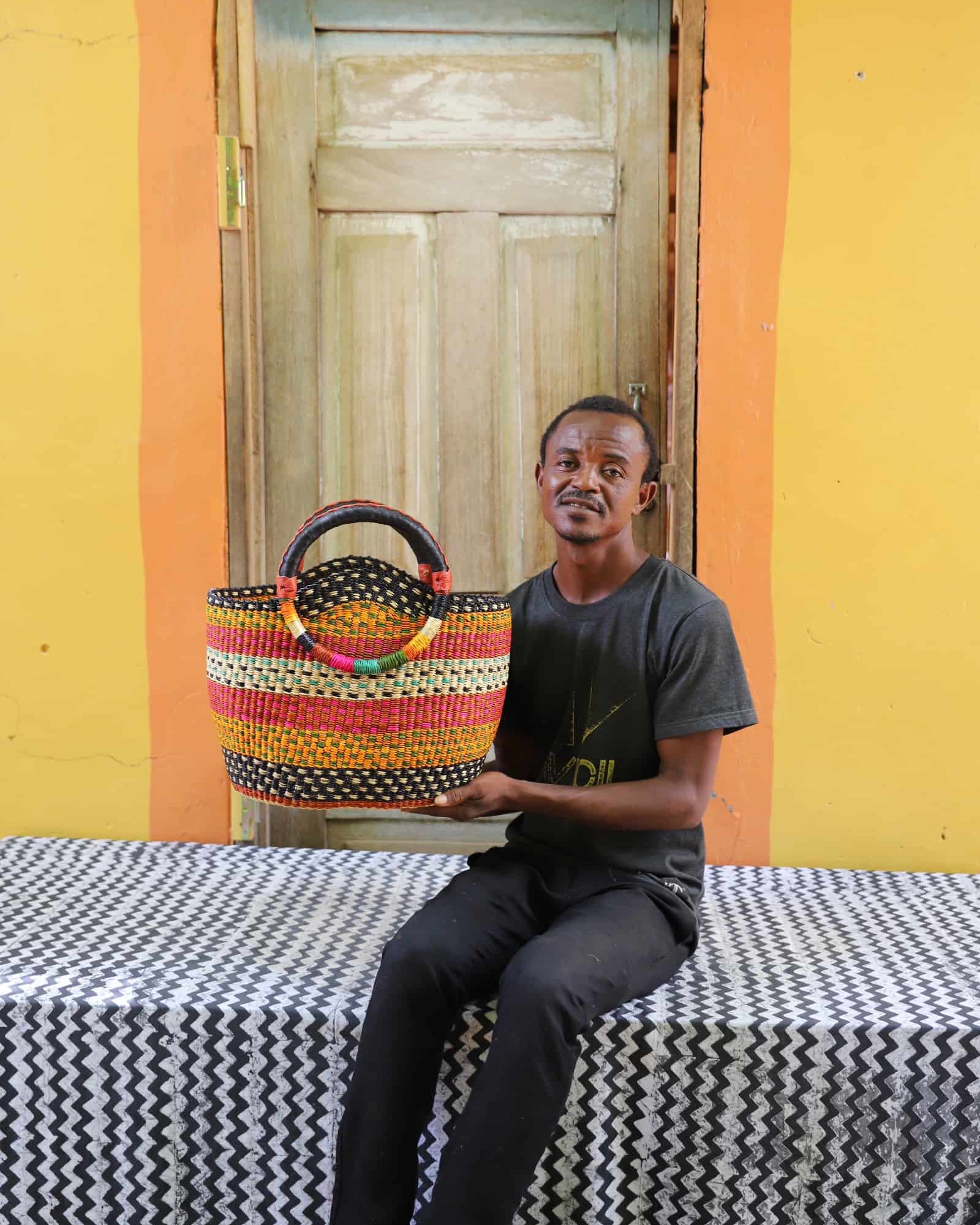 Man holding a colorful woven carry on bag on a black and white cloth against a wooden door.