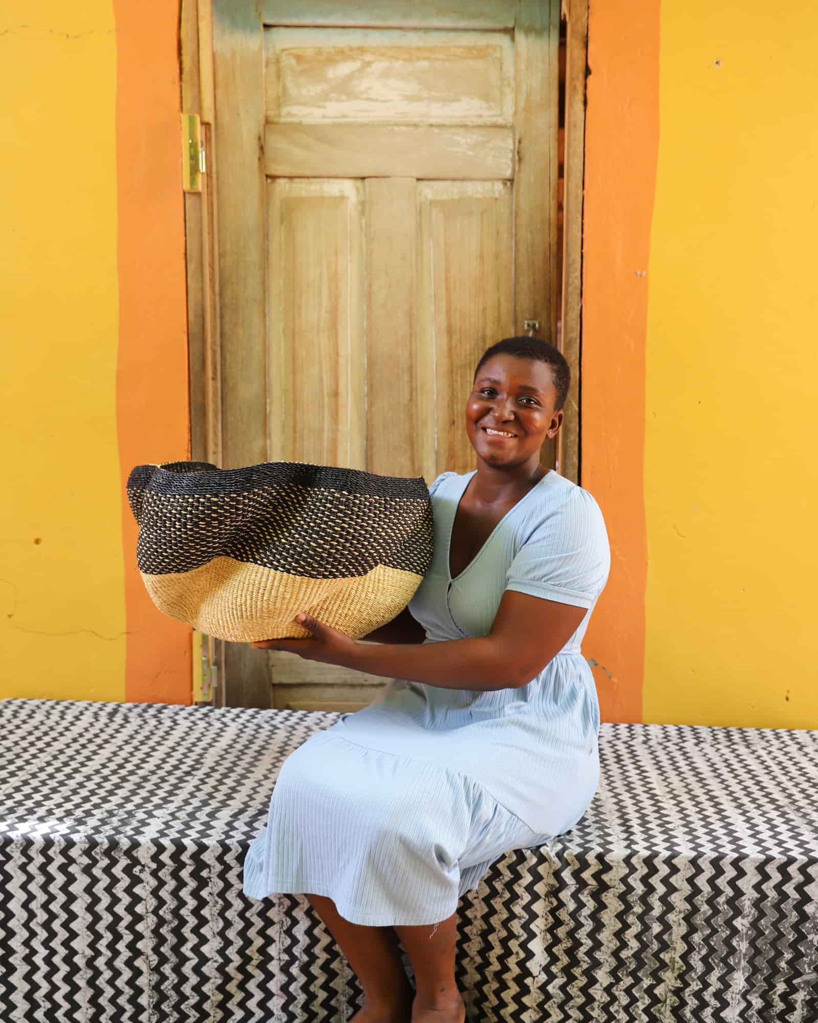 Artisan holding a decorative woven basket on a black and white cloth against a wooden door.