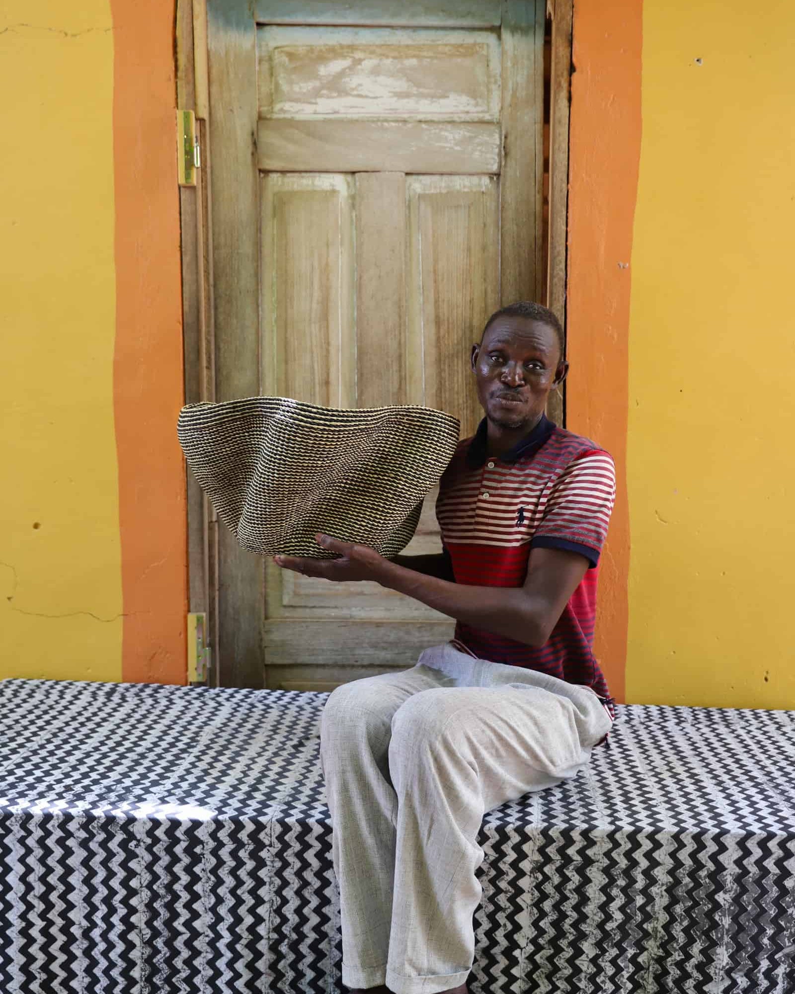 Artisan holding a decorative woven basket on a black and white cloth against a wooden door.