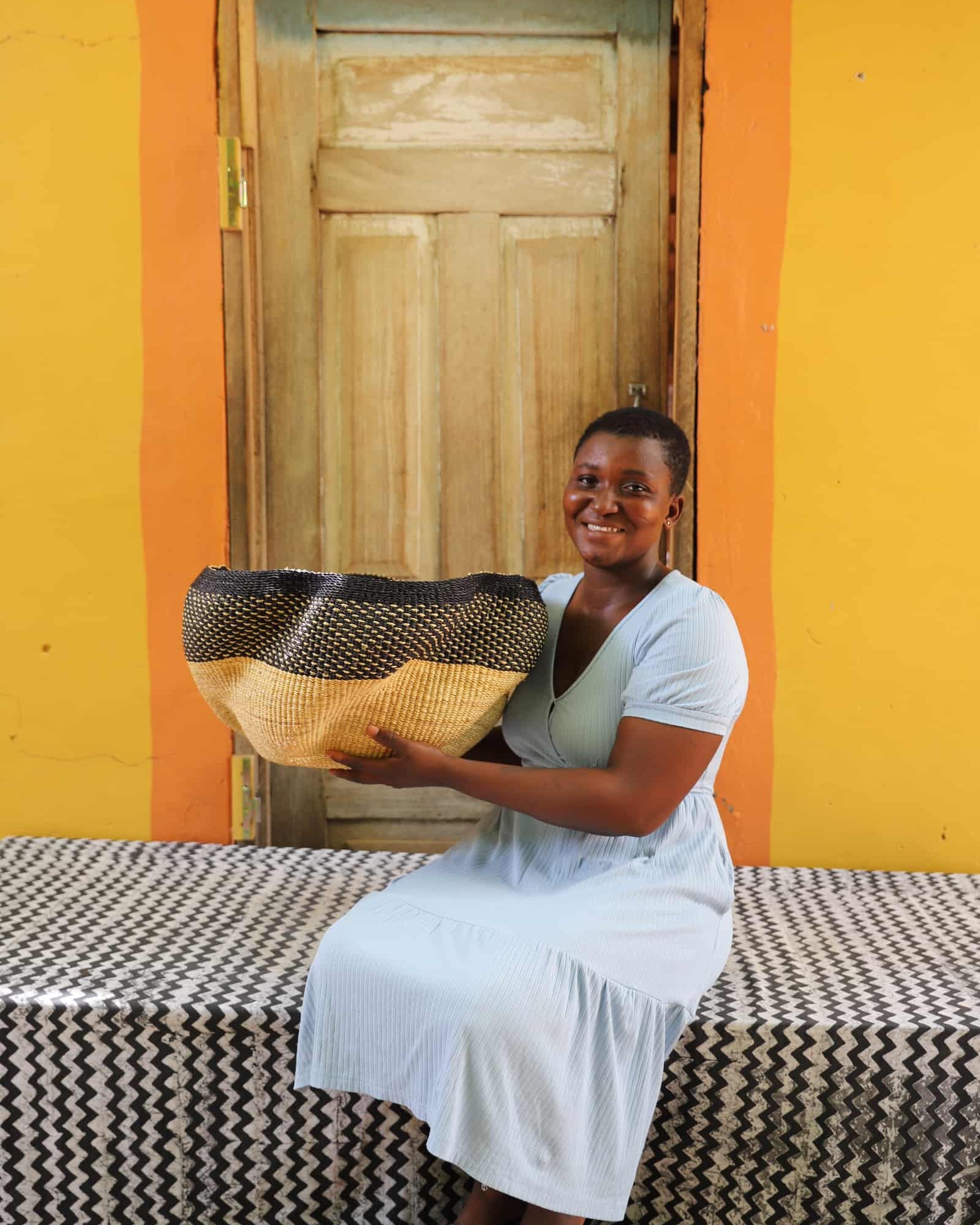 Artisan holding a decorative woven basket on a black and white cloth against a wooden door.