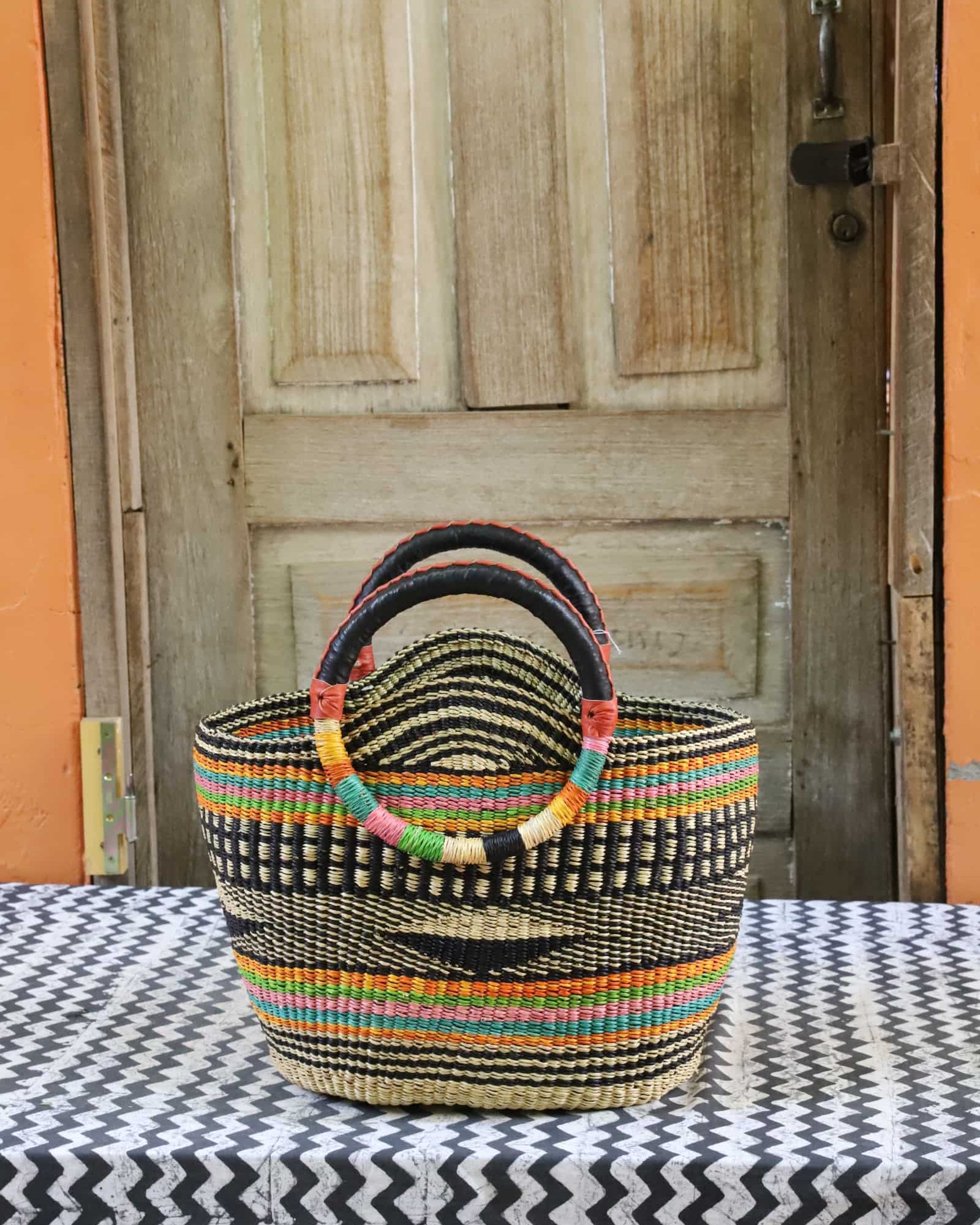 Colorful woven carry on bag on a black and white cloth against a wooden door.