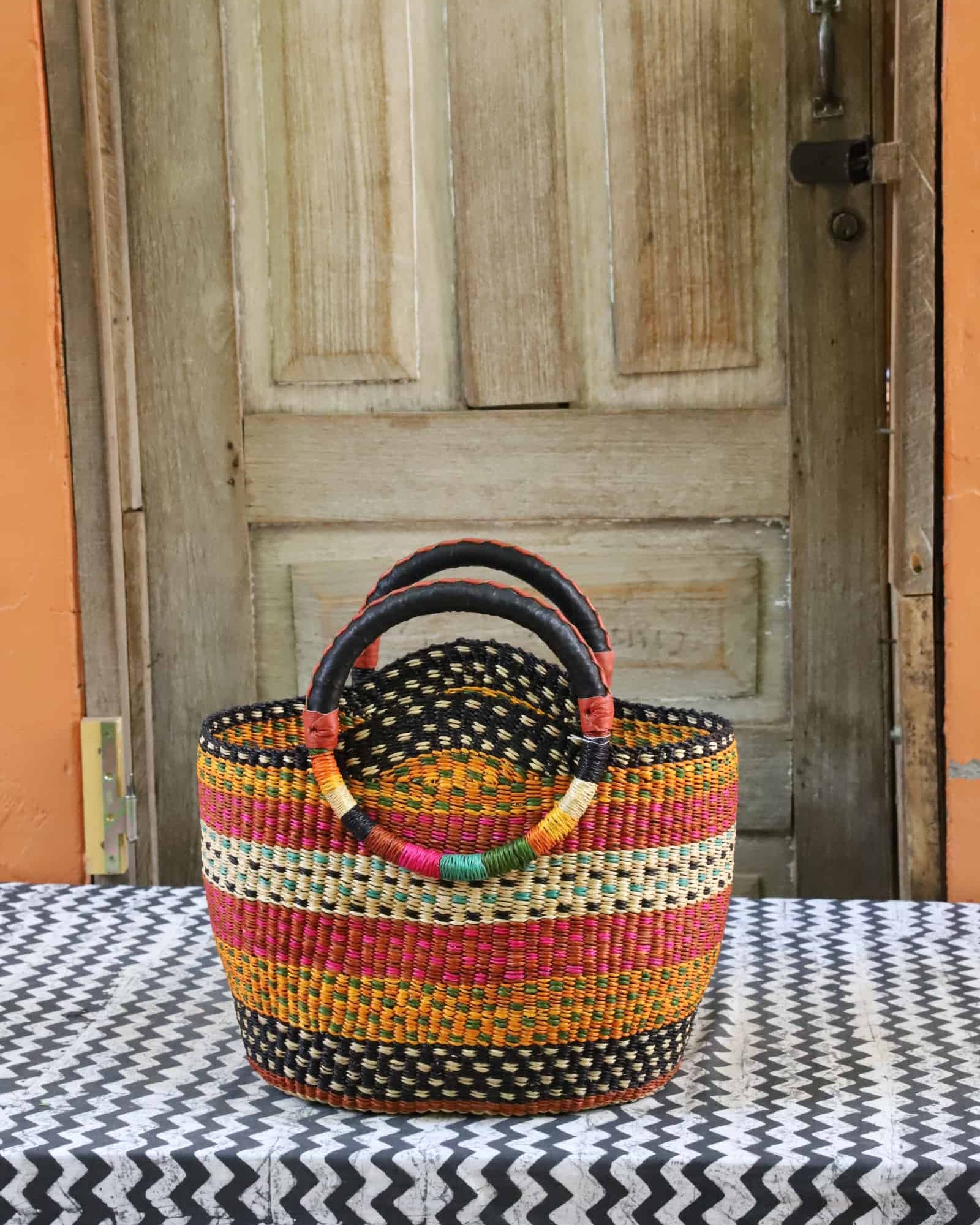 Colorful woven carry on bag on a black and white cloth against a wooden door.