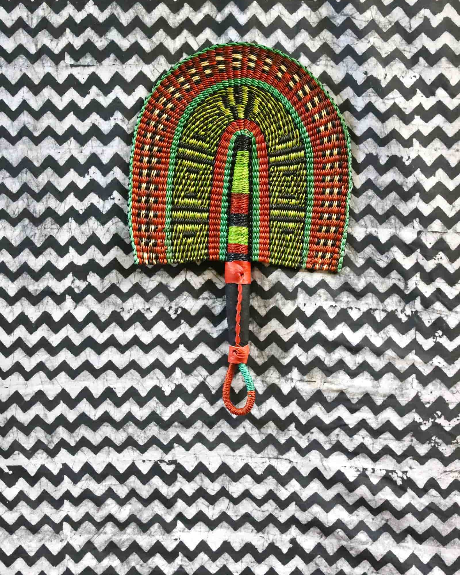 Handwoven Bolga fan with an orange and lime geometric arch pattern, on a black and white chevron cloth.