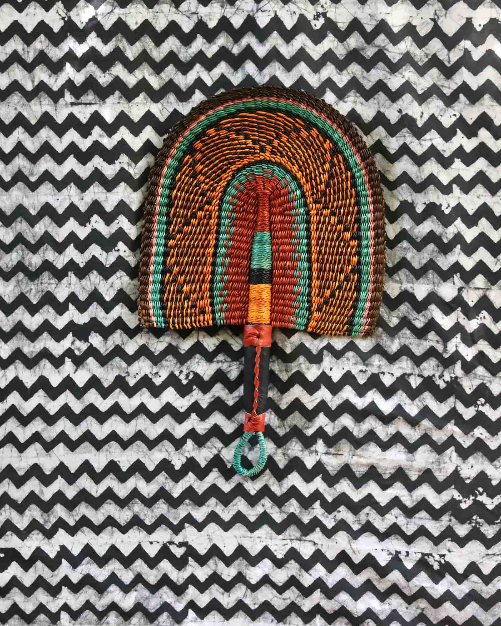 Handwoven Bolga fan with a dark brown body and teal concentric arch outlines, teal loop handle, on a chevron cloth.