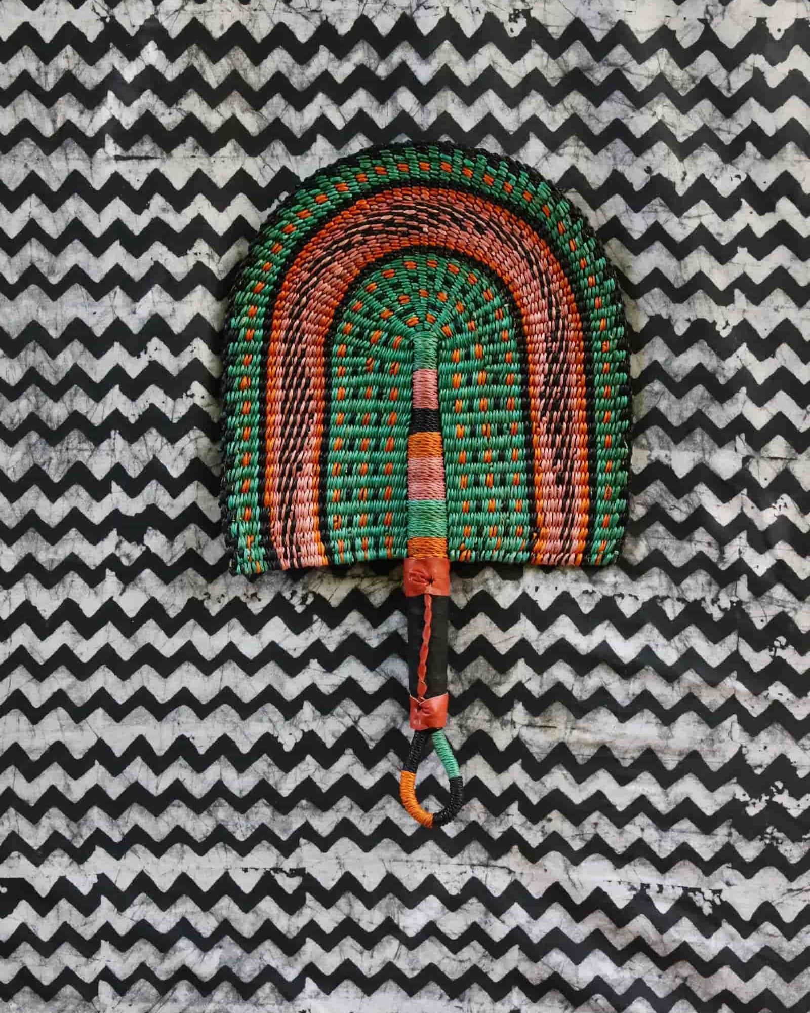 Handwoven Bolga fan in green and terracotta concentric arch, speckled detailing, on a black and white chevron cloth.