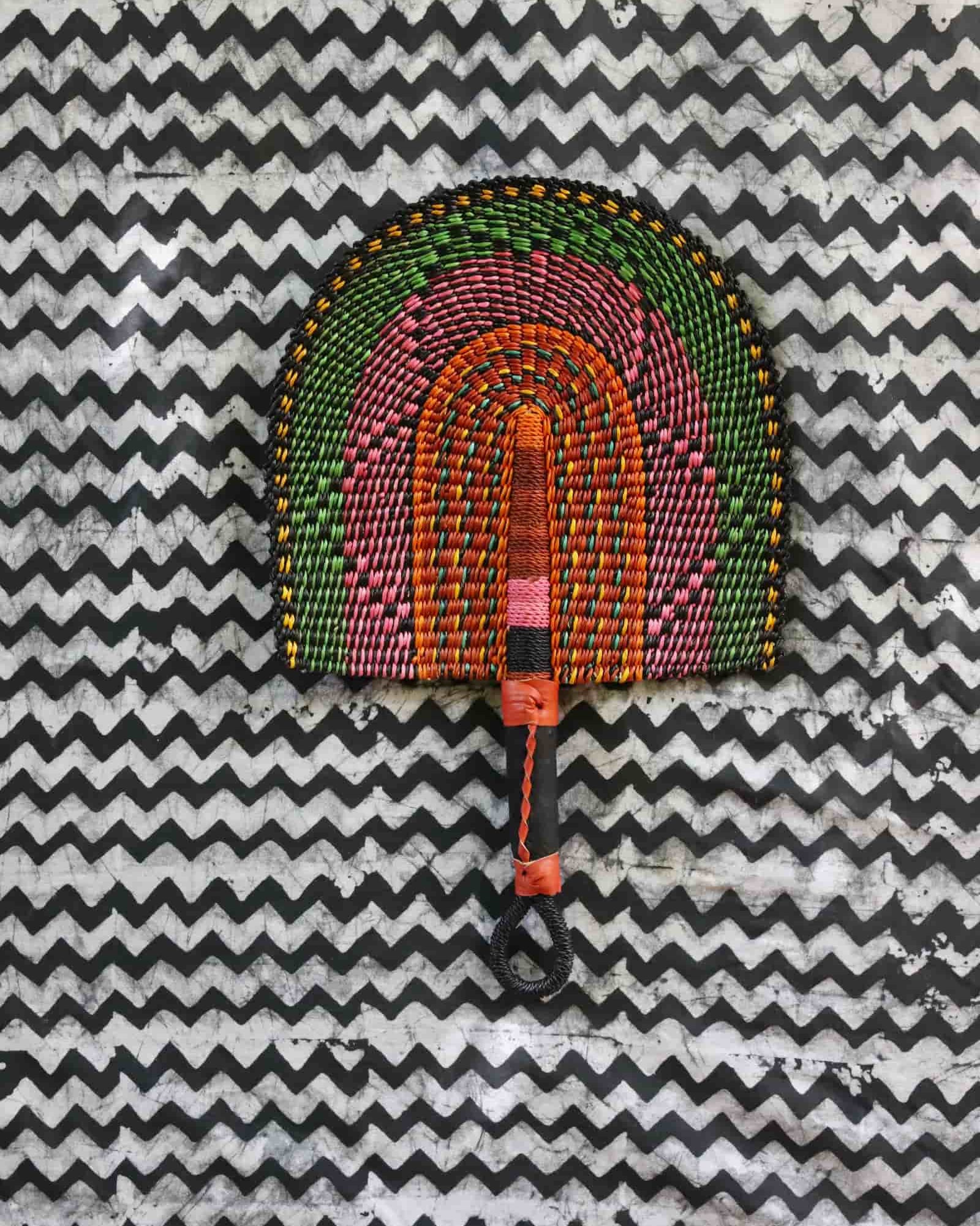 Handwoven Bolga fan with green, pink and amber concentric arch pattern, on a black and white chevron cloth.