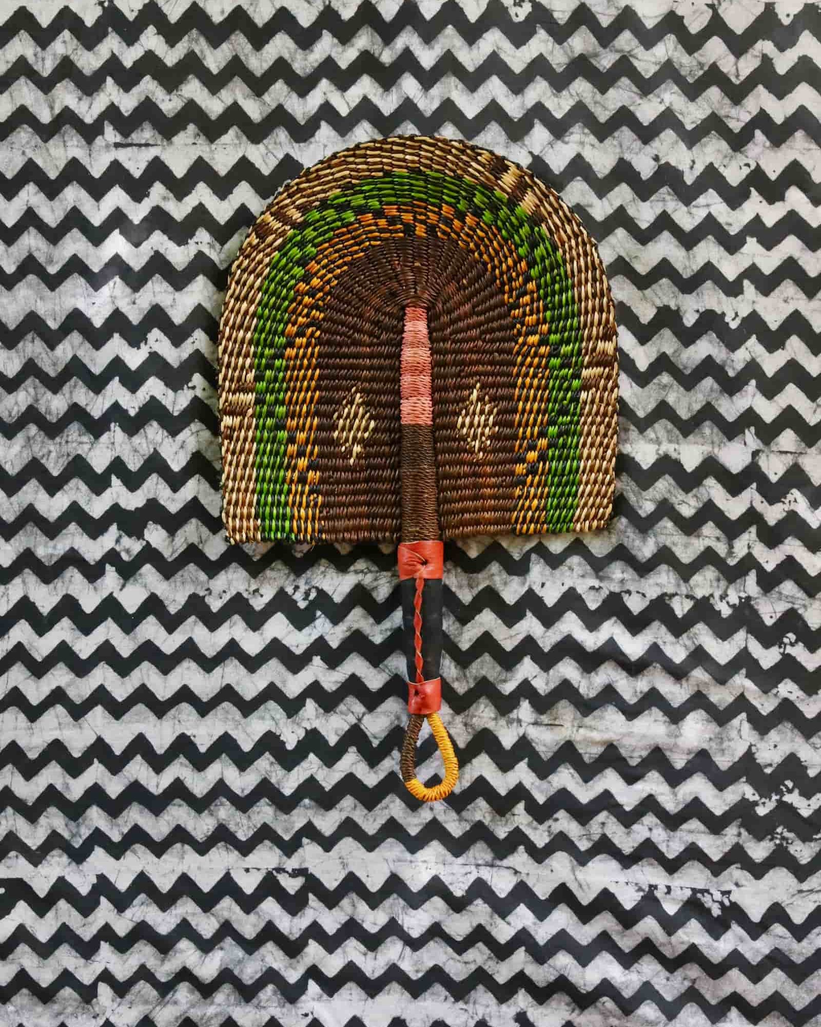 Handwoven Bolga fan in dark brown with green and amber speckled arches, on a black and white chevron cloth.