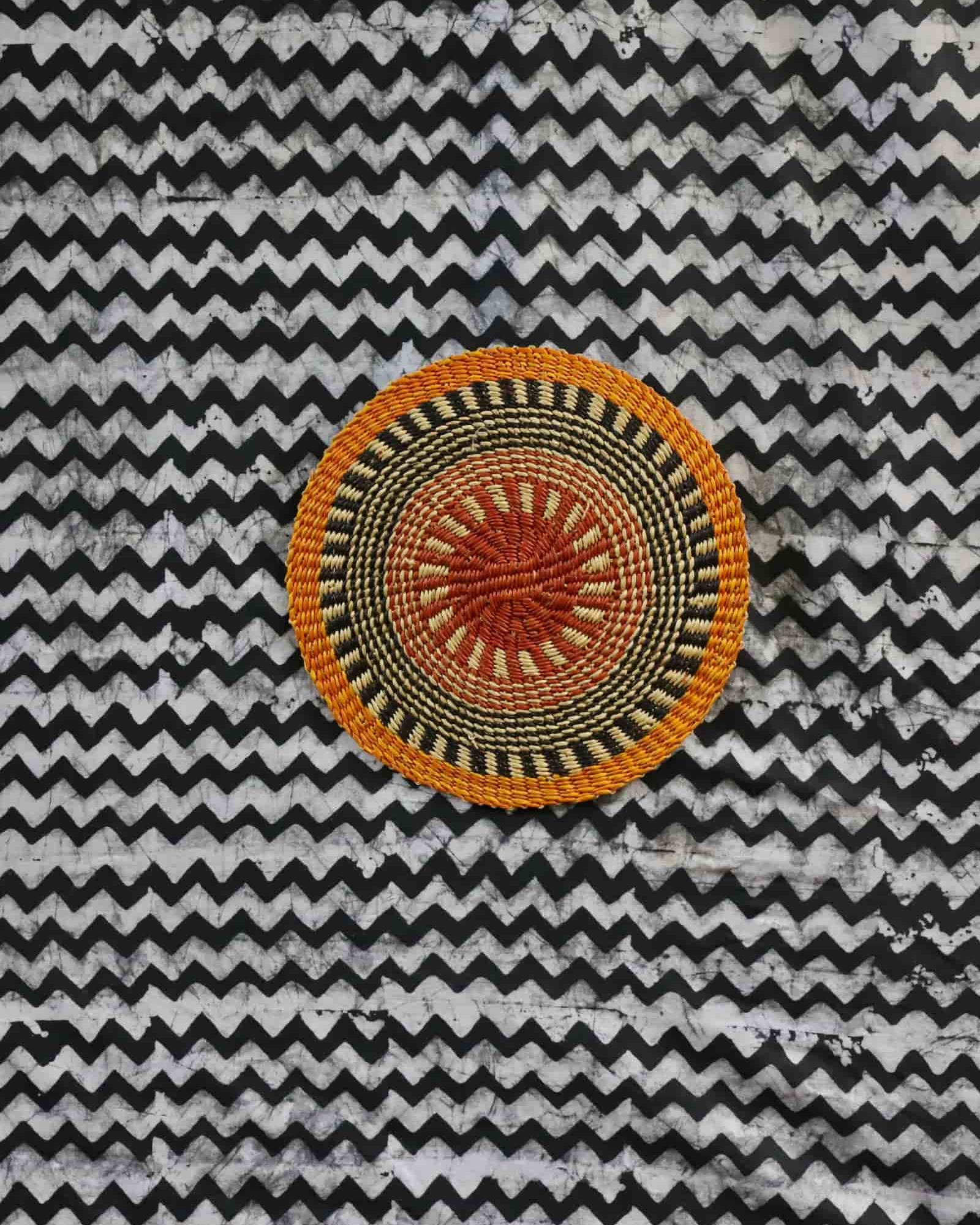 Small woven placemat with terracotta and olive radial pattern, natural straw outer ring