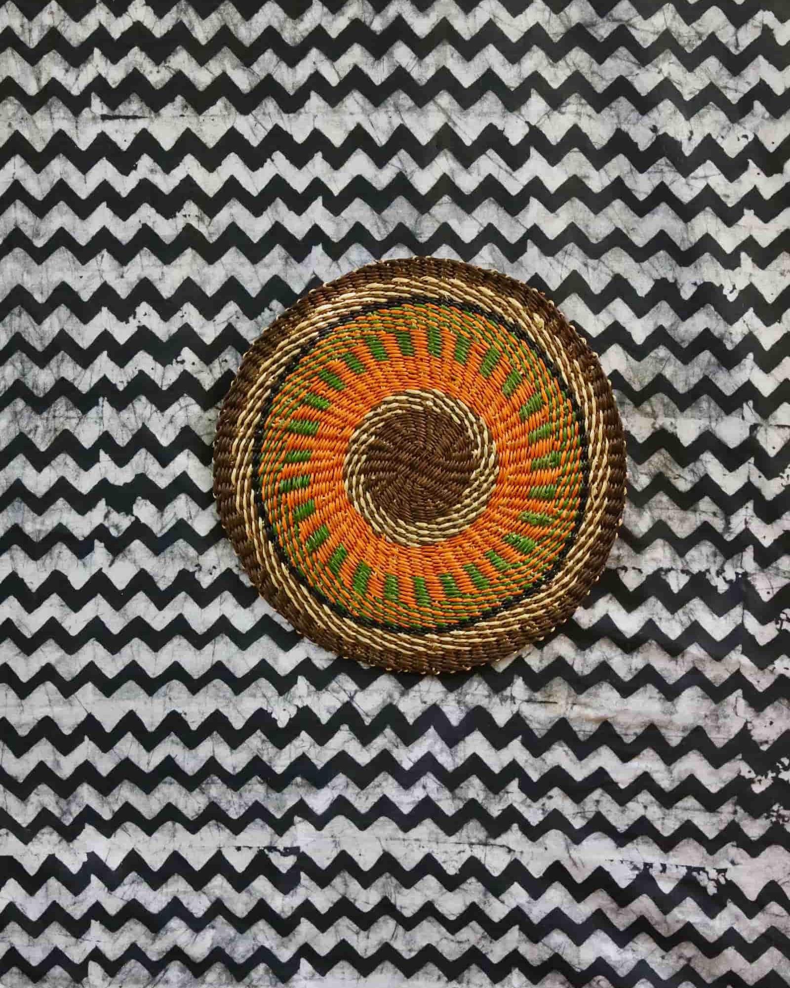 Small woven placemat with orange and green starburst pattern, dark border
