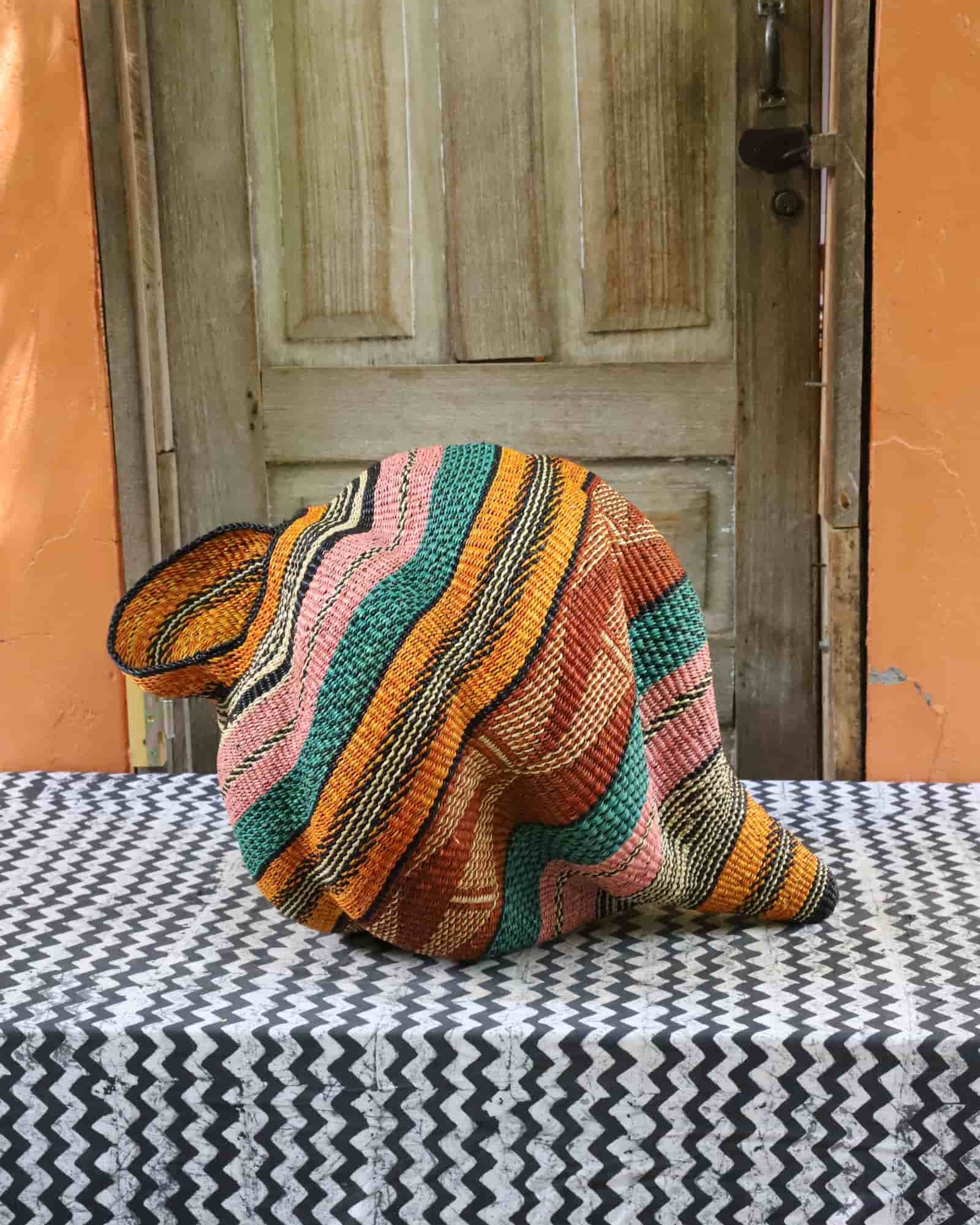 Handwoven Katayeli-tia art basket with teal, amber and pink flowing stripes, on a black and white chevron cloth.