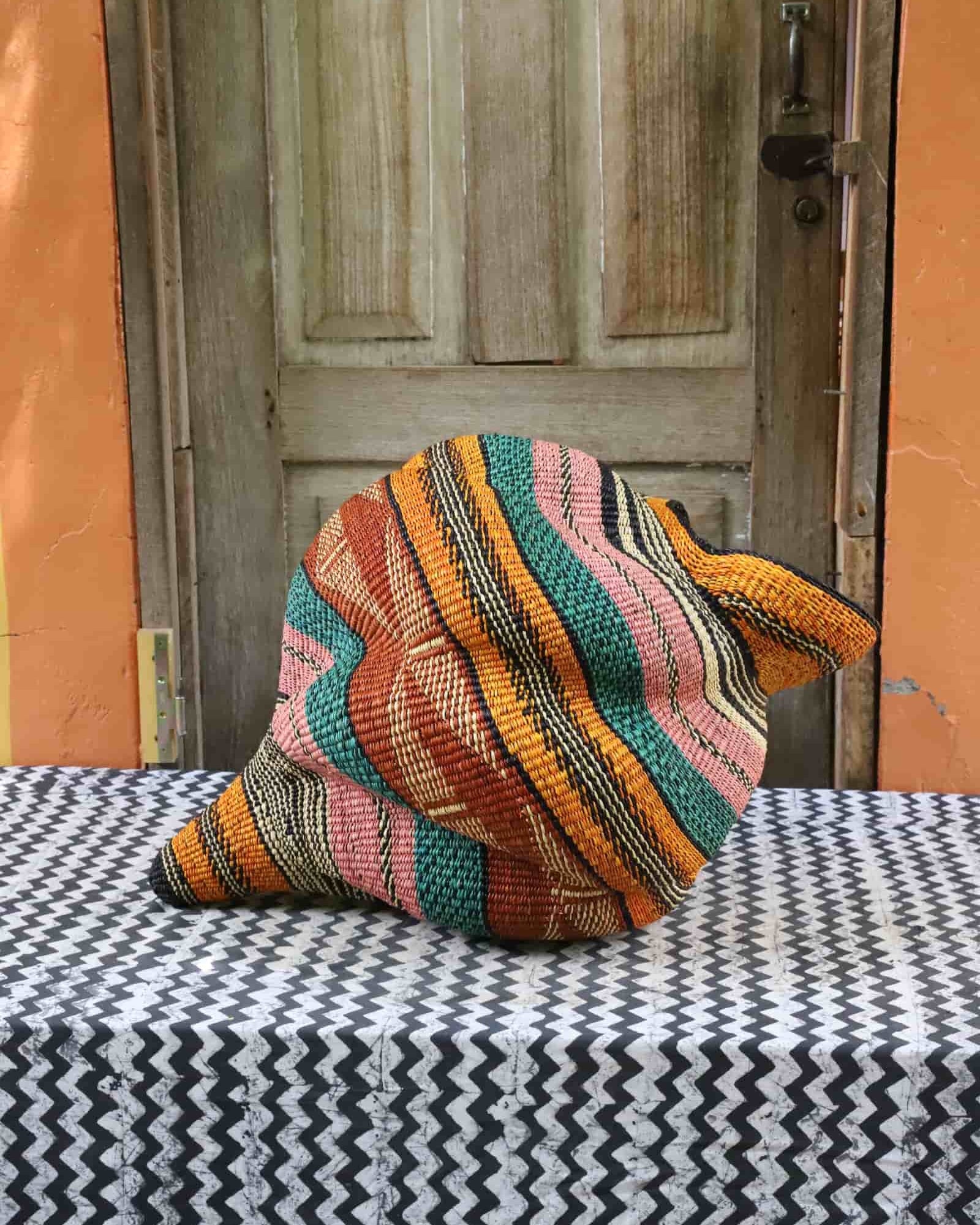 Handwoven Katayeli-tia art basket with teal, terracotta and amber flowing stripes, on a black and white chevron cloth.