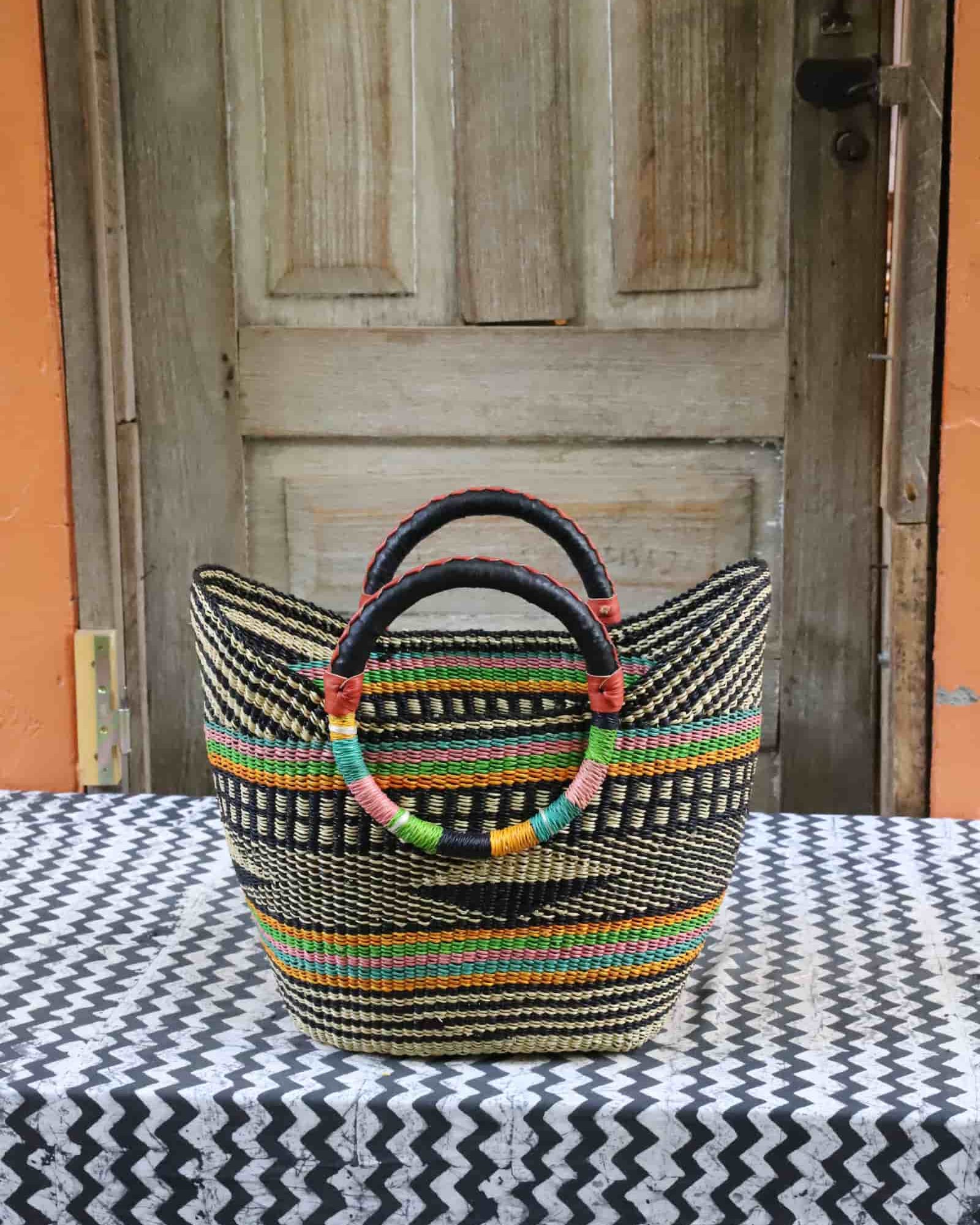 Woven beach bag in black and natural weave with colourful stripe accents and circular leather handles