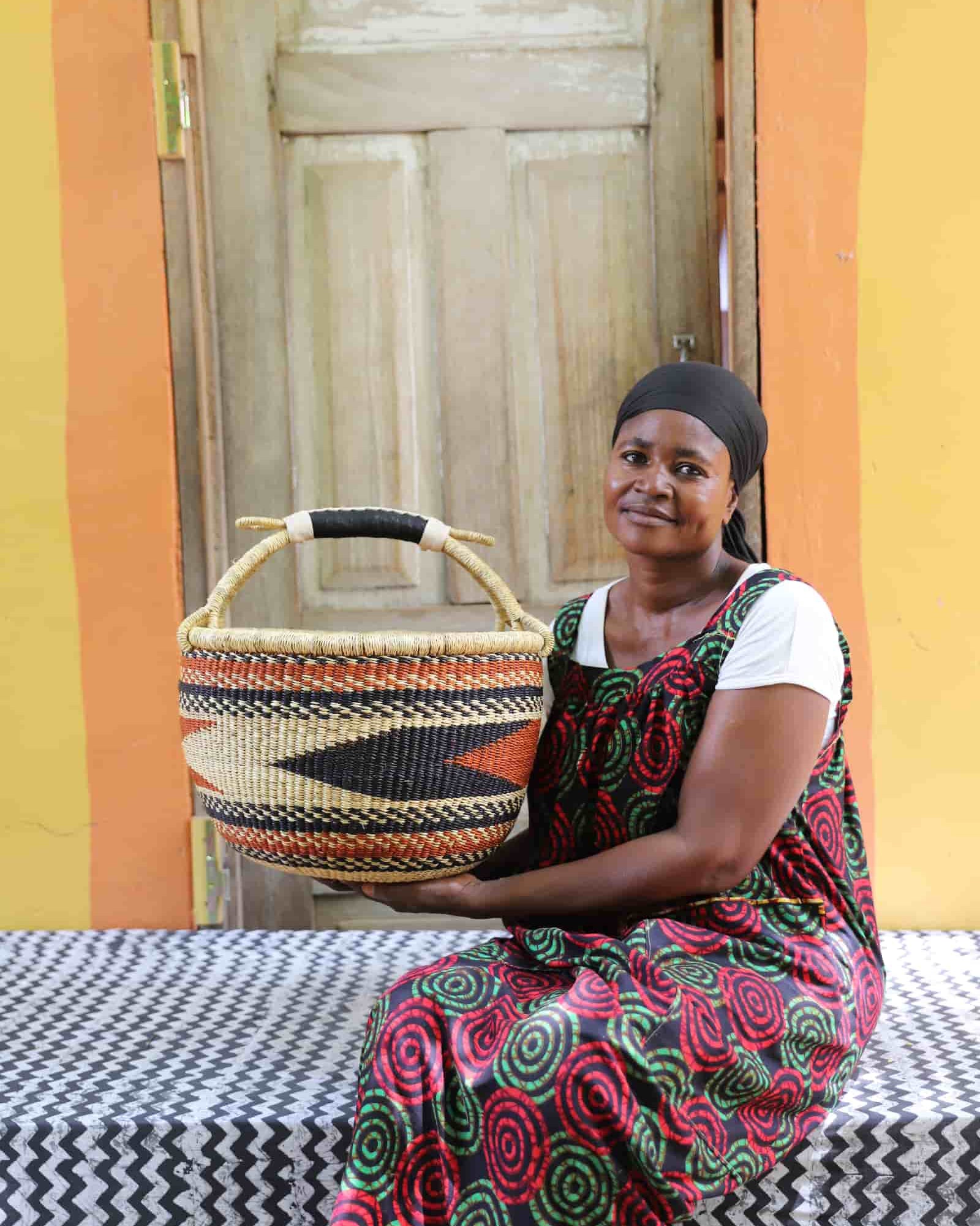 Woman in dark floral African print dress holding a large black and natural patterned Bolga shopping basket