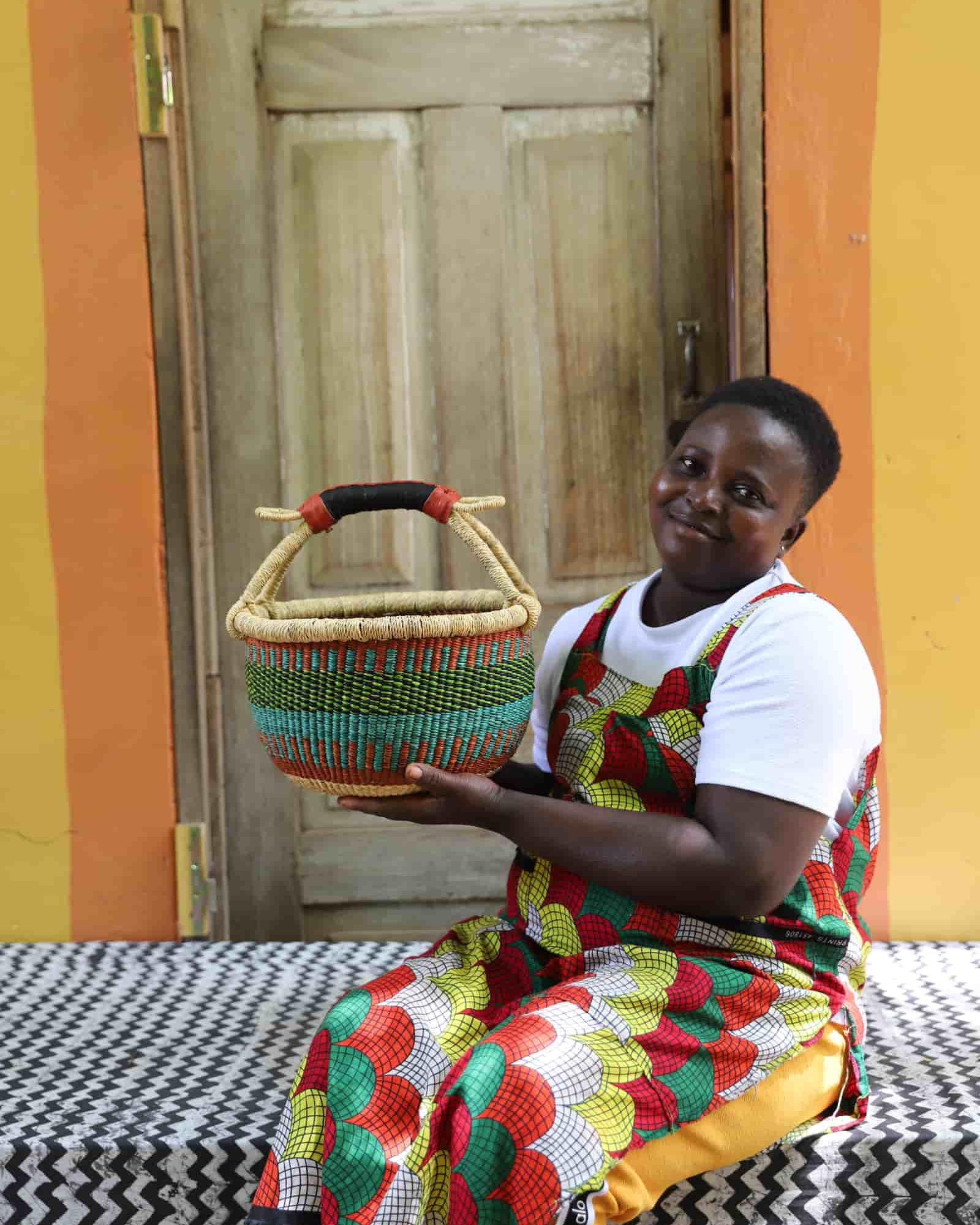 Woman in colourful African print dress holding a small green and teal Bolga shopping basket